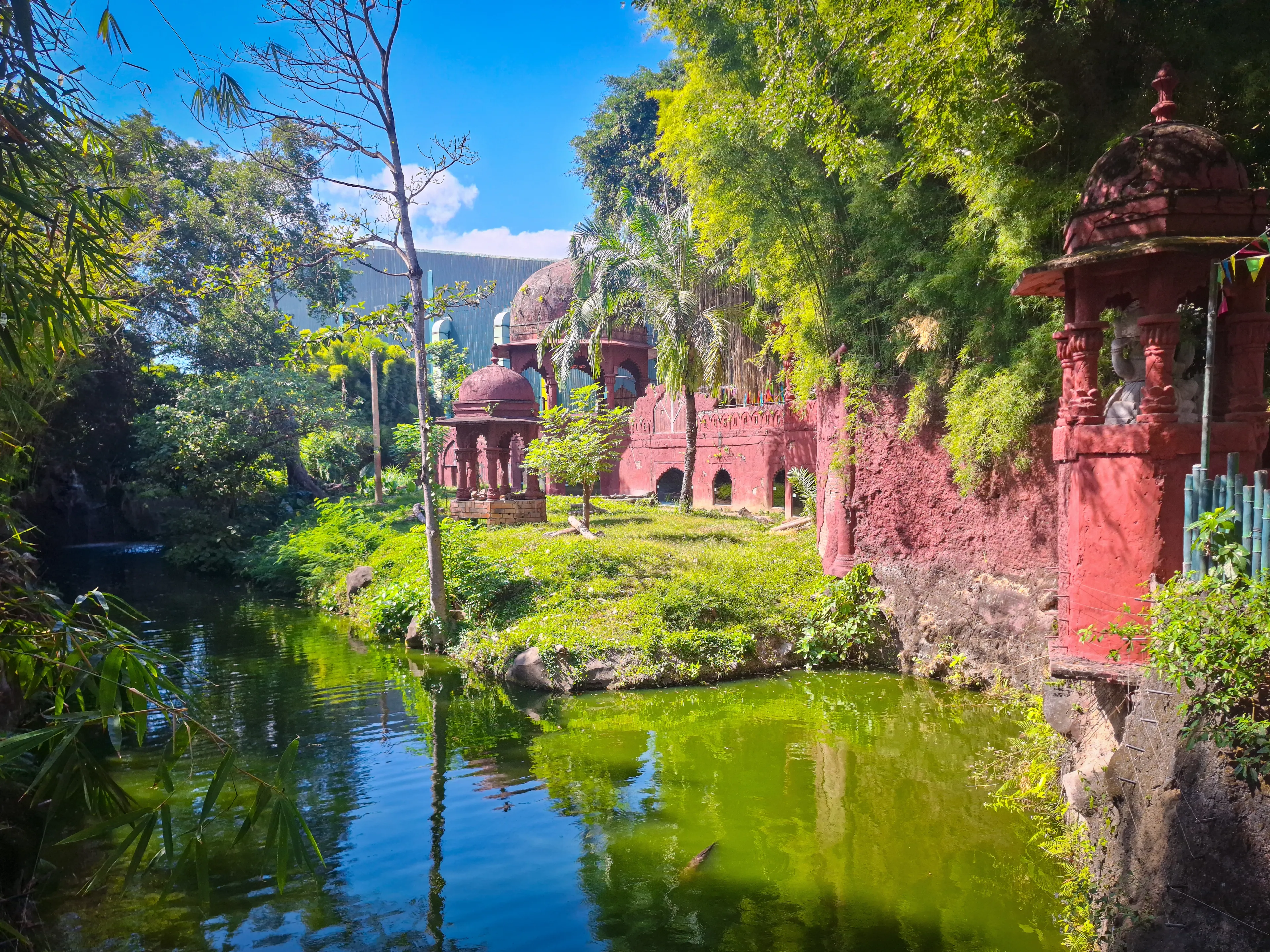Gianyar, Indonesia - July 16th 2024: Serene view of Taman Safari Bali's white tiger exhibit, featuring ancient-inspired red brick structures alongside a tranquil green pond and lush tropical foliage