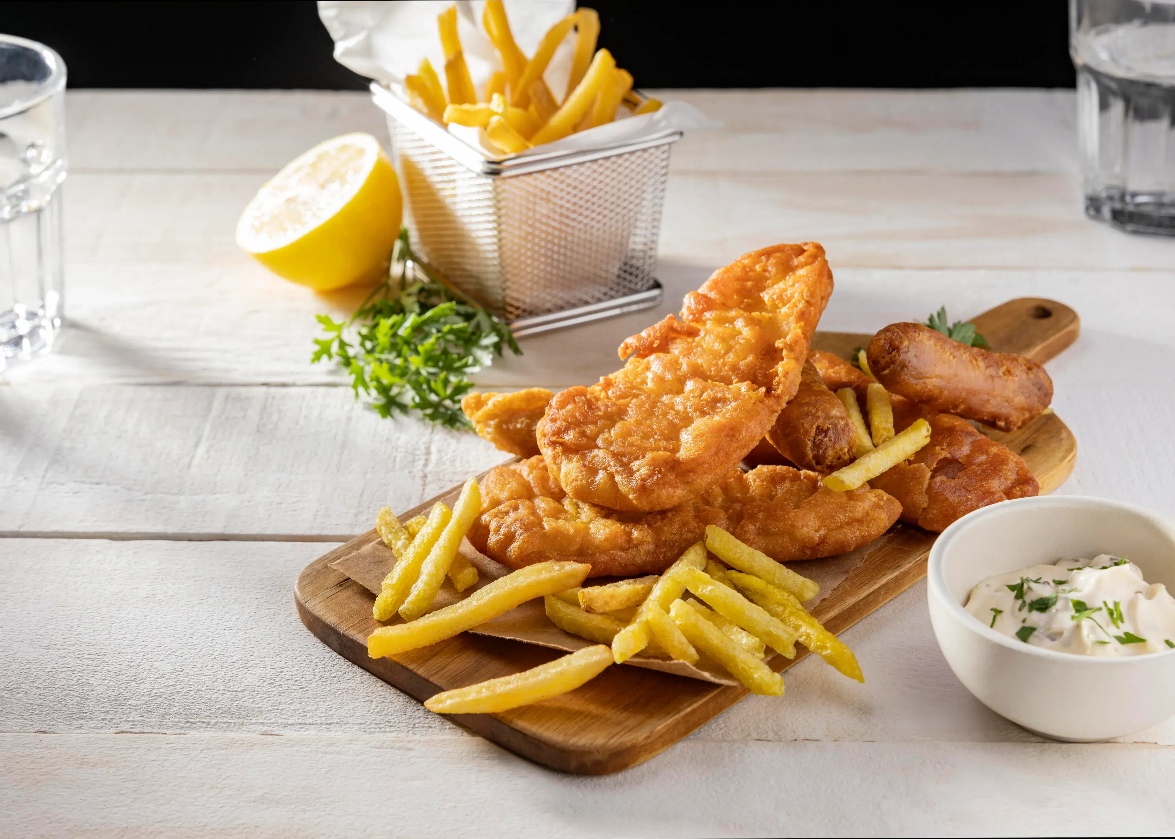 Fish and chips on chopping board with lemon and sauce Fish and chips on chopping board with lemon and sauce