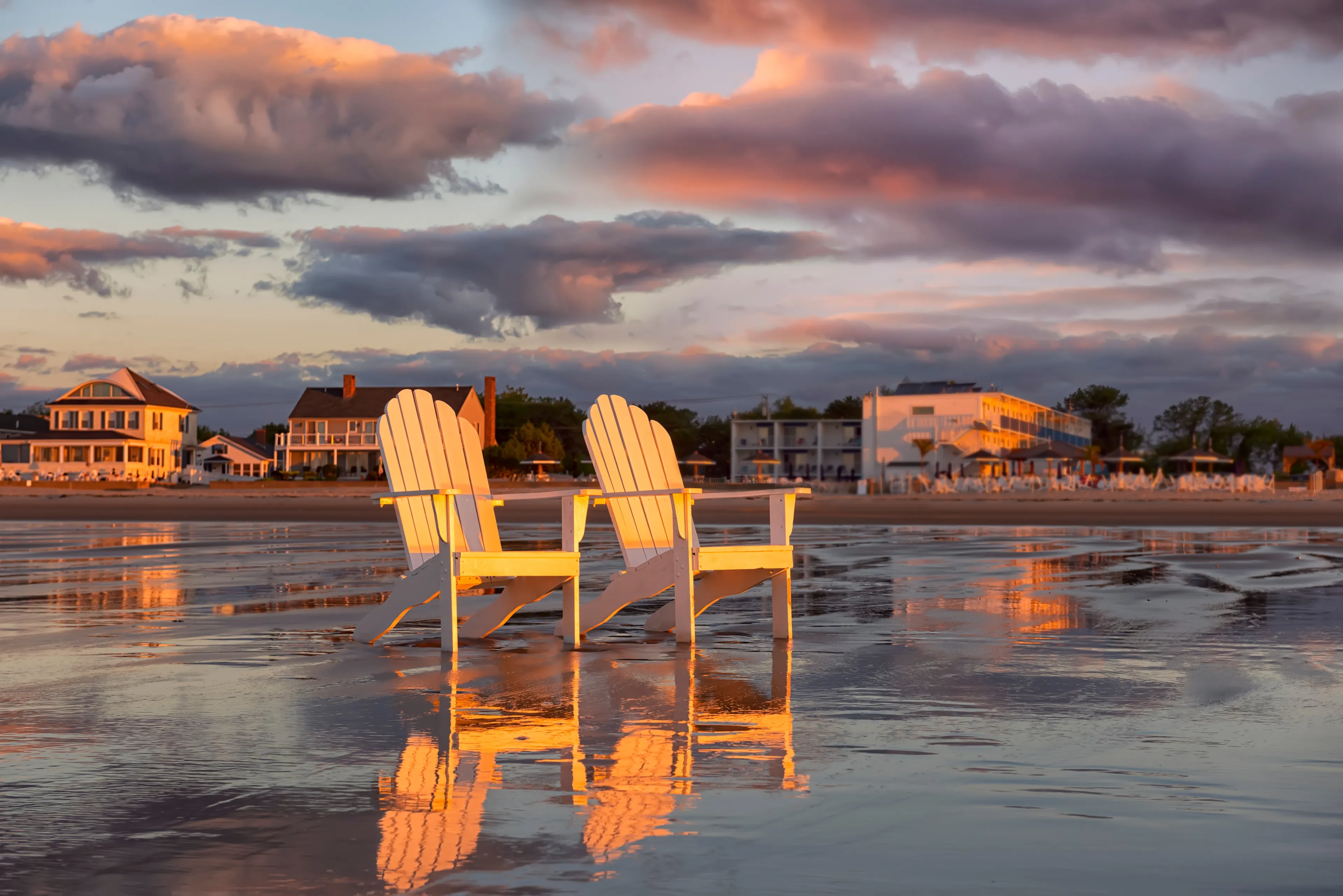 Two wooden traditional armchairs on a sandy beach at sunrise overlooking the coastline. Atlantic Ocean. USA. Maine. Old Orchard Beach.