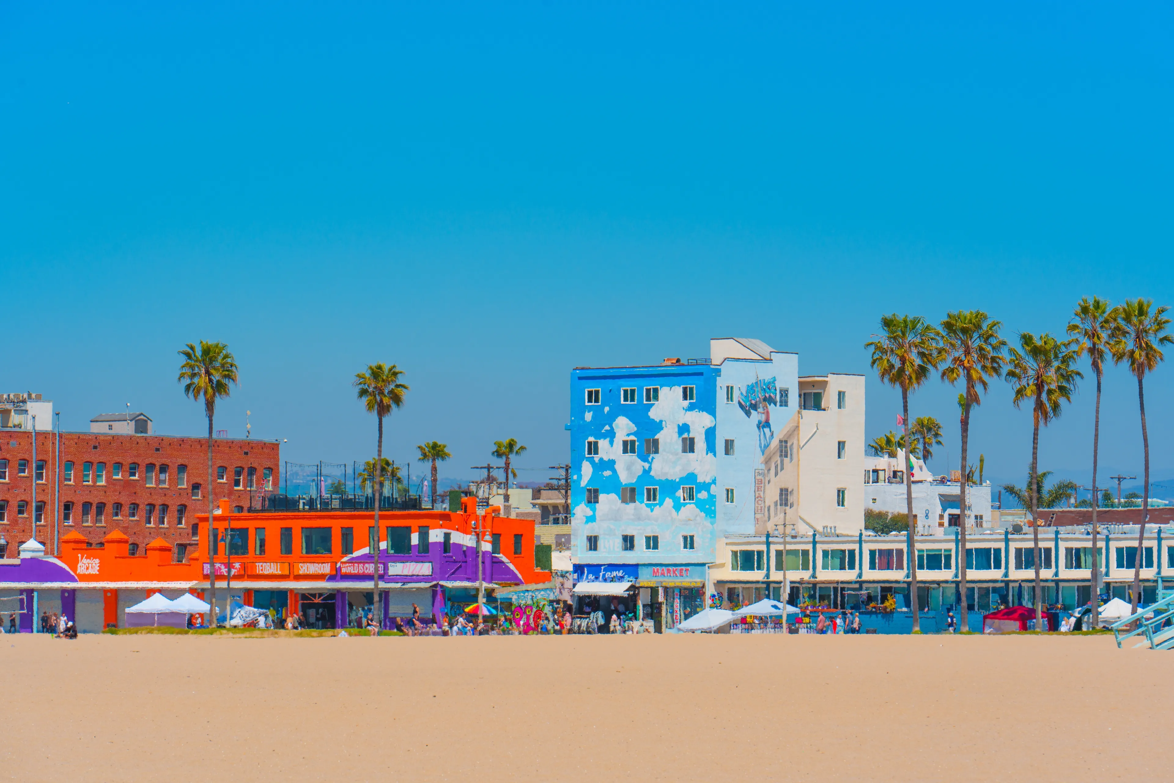 Los Angeles, California - April 3, 2024: View from Venice Beach showcasing colorful buildings and market stalls along the beach line against a clear blue sky