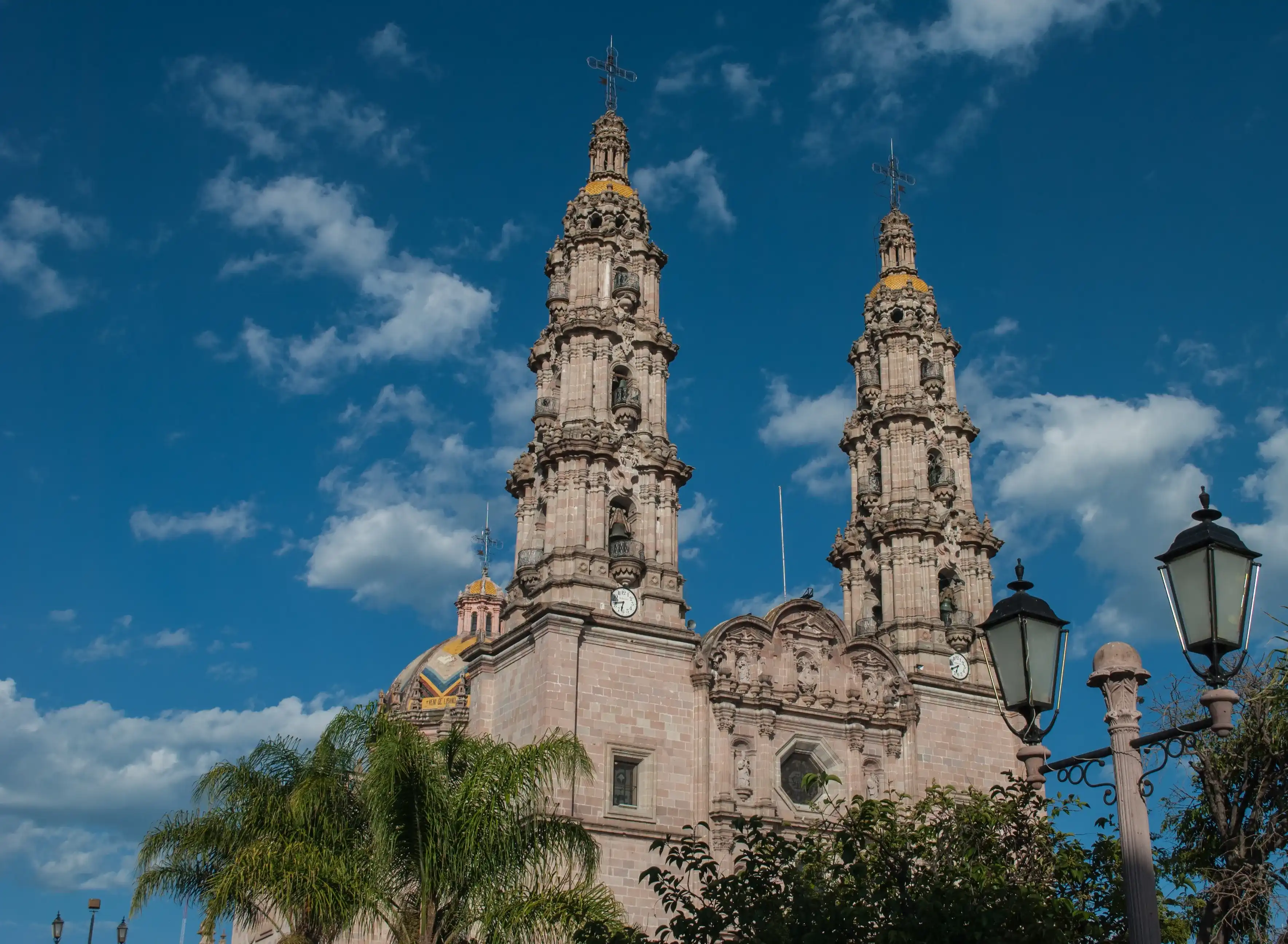 The Cathedral/Basilica of the Virgin of San Juan de los Lagos pink sandstone with two narrow Baroque towers and a portal with three levels and a crest, blue sky background The Cathedral/Basilica of the Virgin of San Juan de los Lagos pink sandstone with two narrow Baroque towers and a portal with three levels and a crest, blue sky background