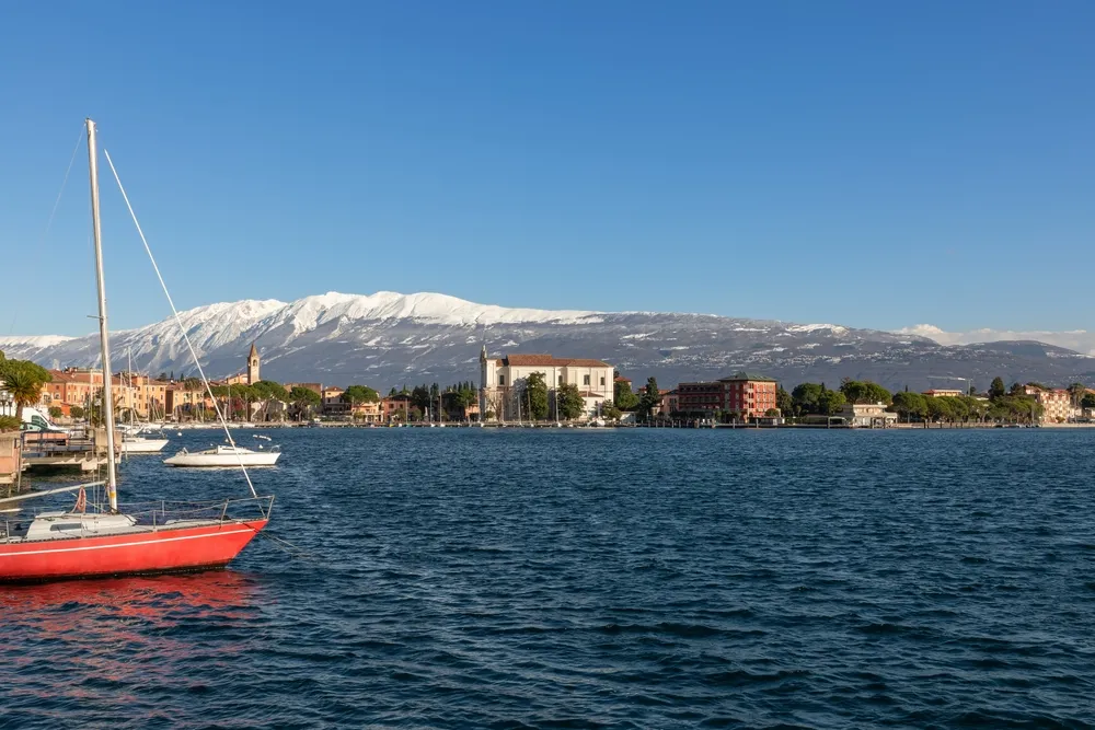 Embankment of the town Moniga del Garda on lake Garda against the background of the Alpine mountains with snow-capped peaks