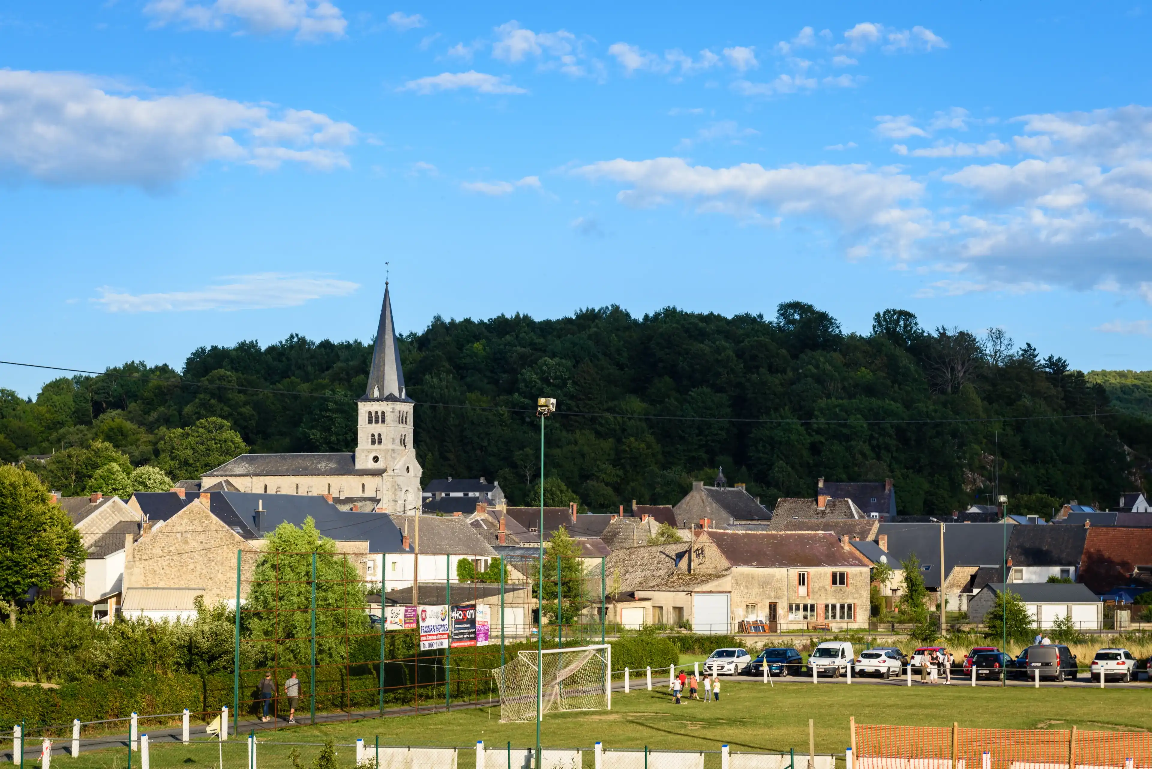 PETIGNY, COUVIN, WALLONIA, BELGIUM - JULY 29, 2017: Small countryside town of Petigny with church tower and football field with hill in background on July 29 in Petigny, Couvin, Wallonia in Belgium.