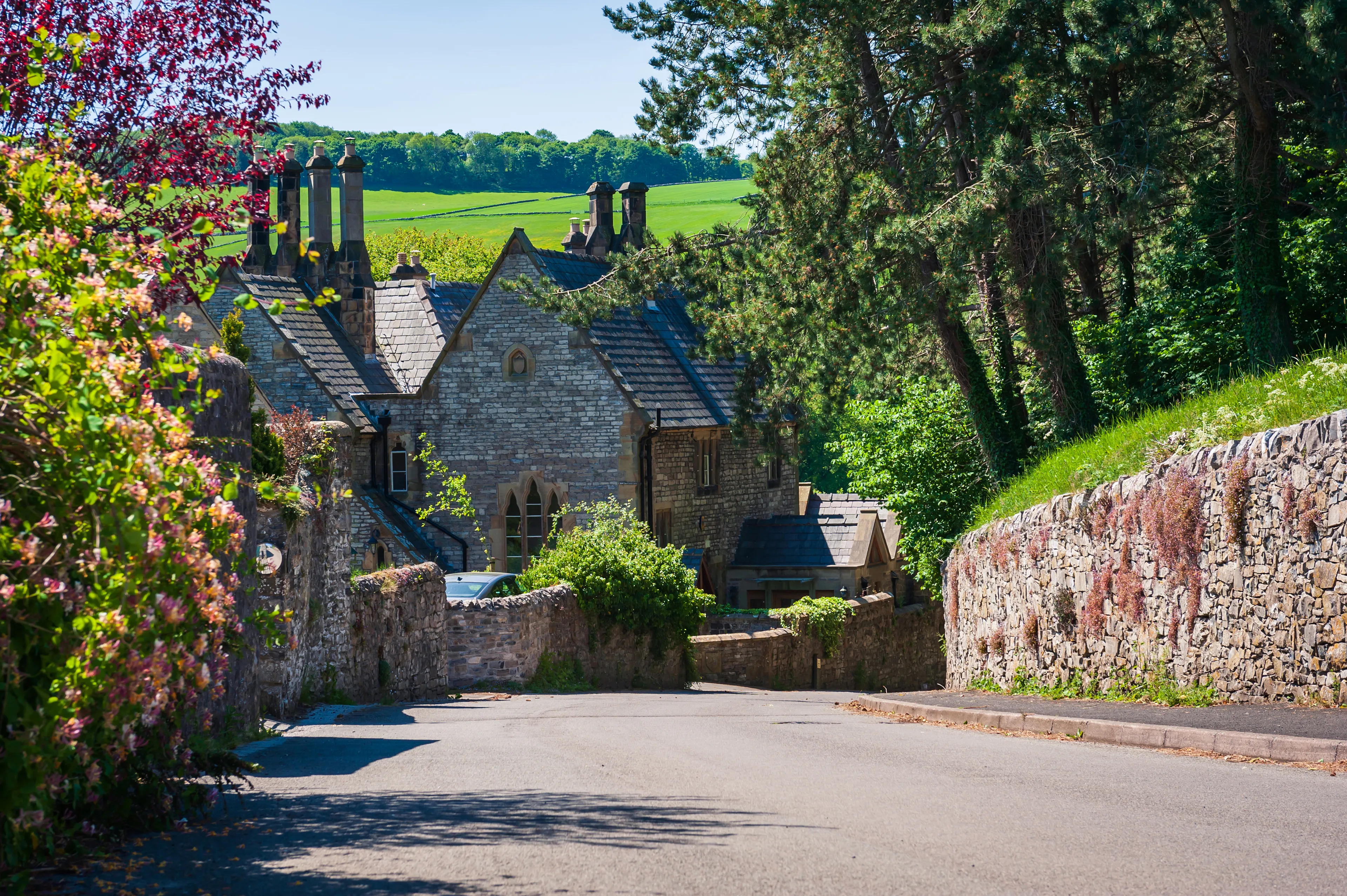 Old stone cottages and trees along the road. Countryside landscape of small village Ashford-in-the-Water in Derbyshire Peak District, England.