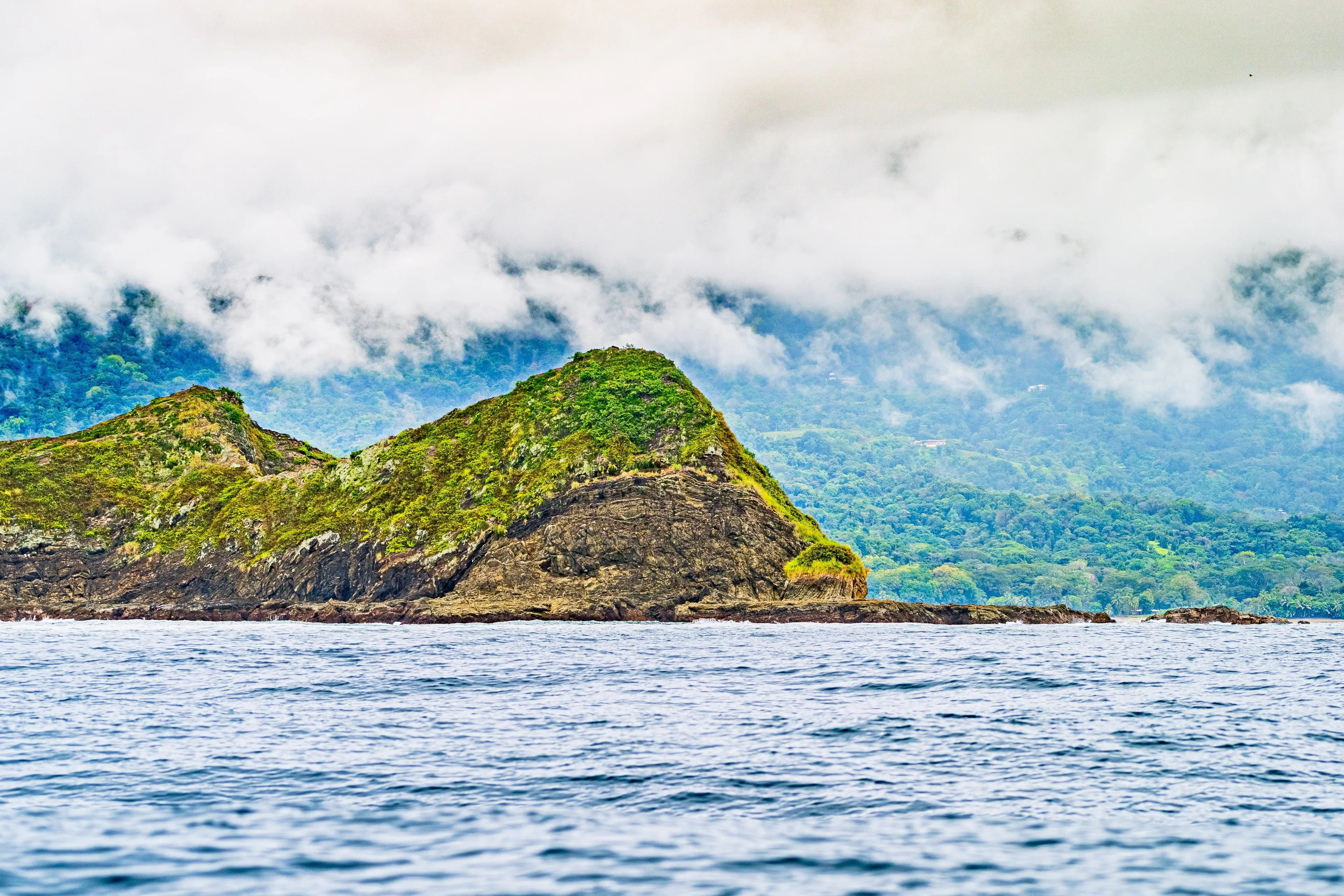 Misty coastal landscape with rugged hills covered in greenery, waves crashing against the rocky shore, and forested mountains in the background. Uvita Puntarenas Province Costa Rica. Pacific Cost.