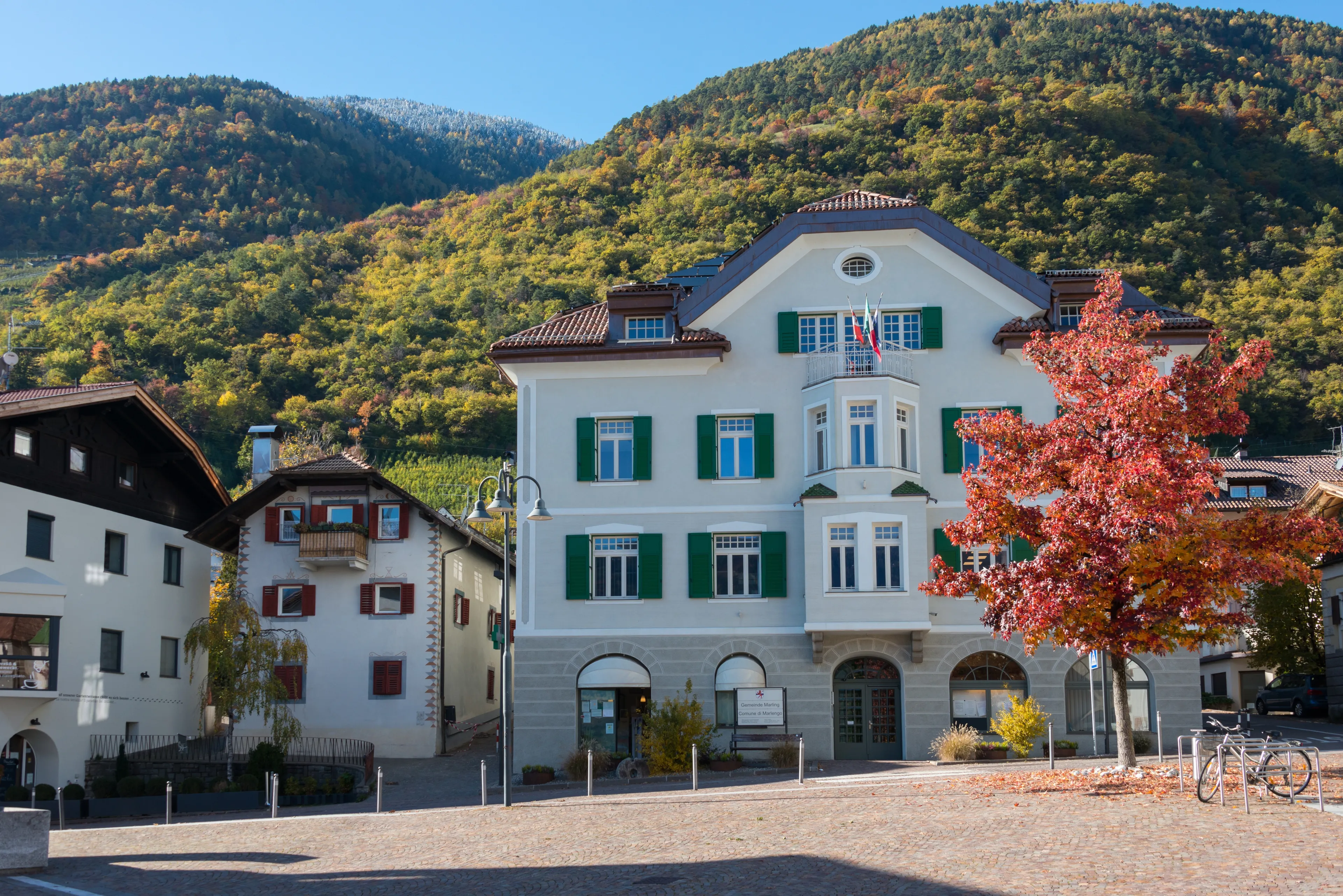 Bolzano, Italy - November 05, 2021: Backlit view of ancient and stately buildings in the square and parish church of the town of Marlengo or Marling in the Trentino-Alto Adige region