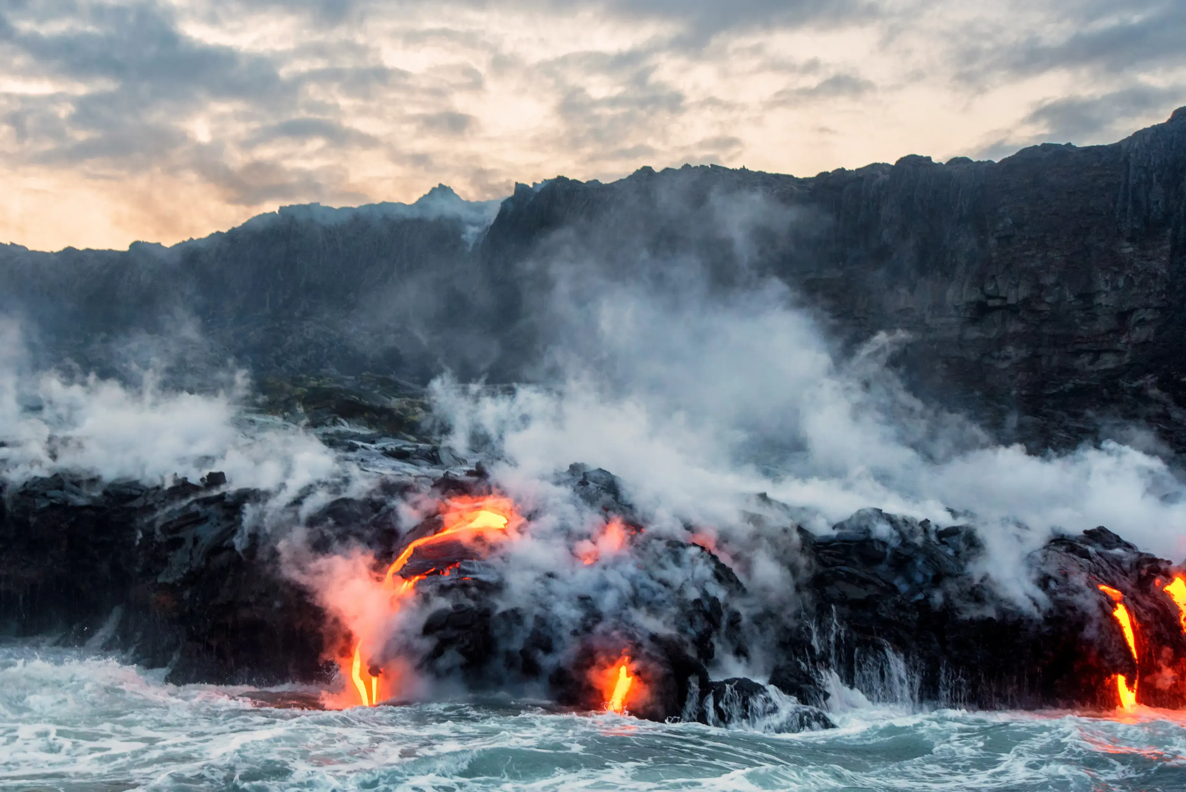 Molten lava flowing into the Pacific Ocean on Big Island of Hawaii, as ocean waves splash onto the rocks and flowing lava Molten lava flowing into the Pacific Ocean on Big Island of Hawaii, as ocean waves splash onto the rocks and flowing lava