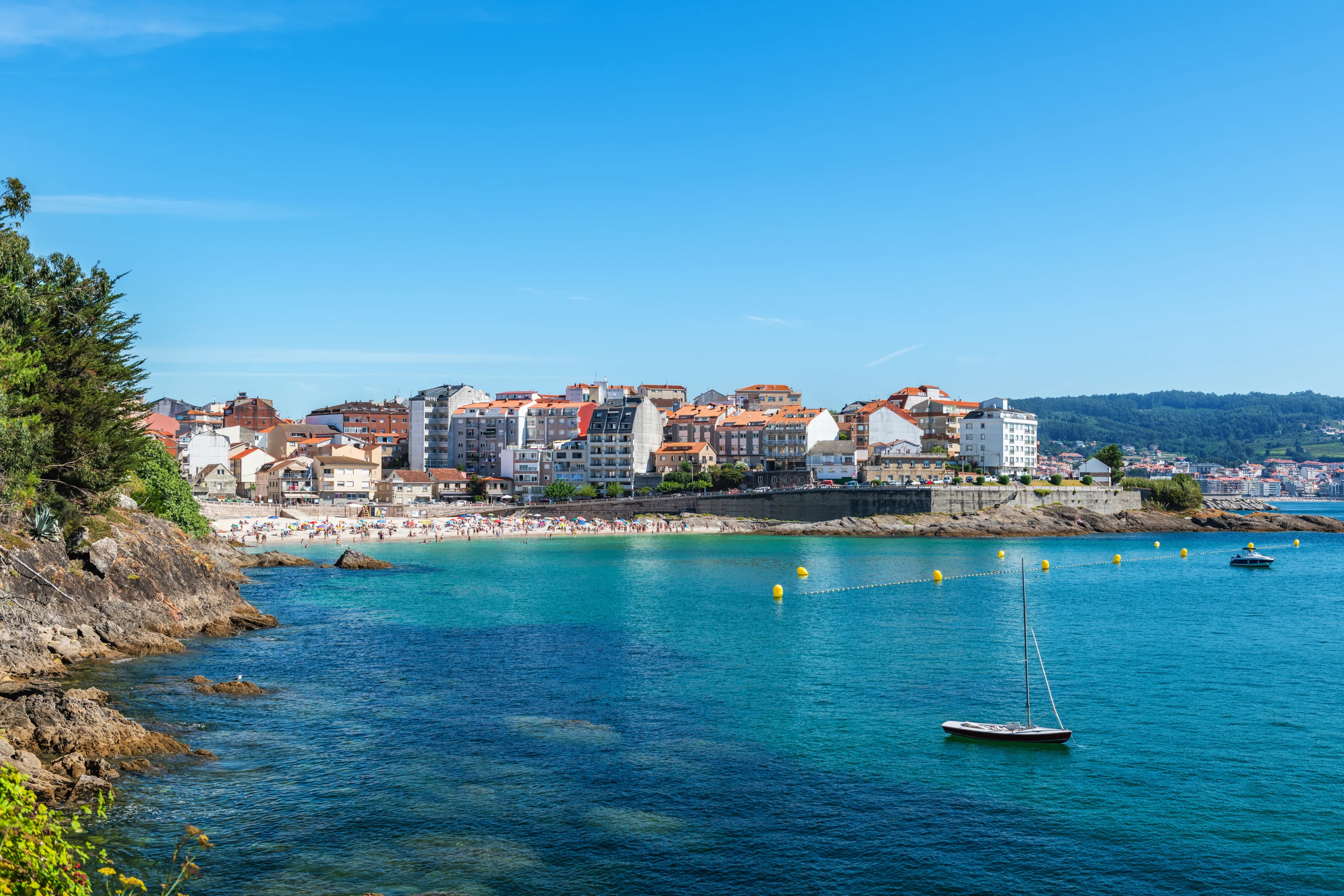 Wide-angle view of a beautiful crowded beach in Portonovo in the Ria de Pontevedra, Spain, on a sunny summer morning with a clear blue sky.