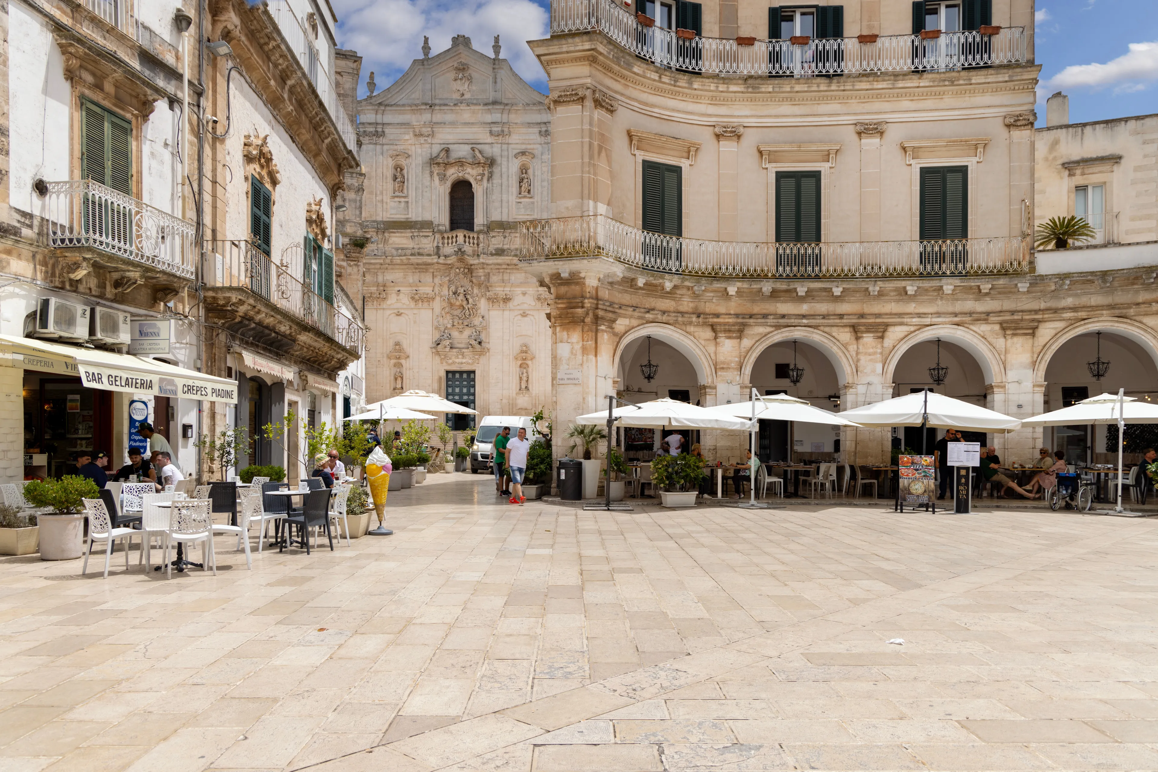 Martina Franca, Italy, Apulia - May 25, 2024: Maria Immaculate Square (Piazza Maria Immacolata), historical portici in neoclassical style. Basilica of San Martino in a distance