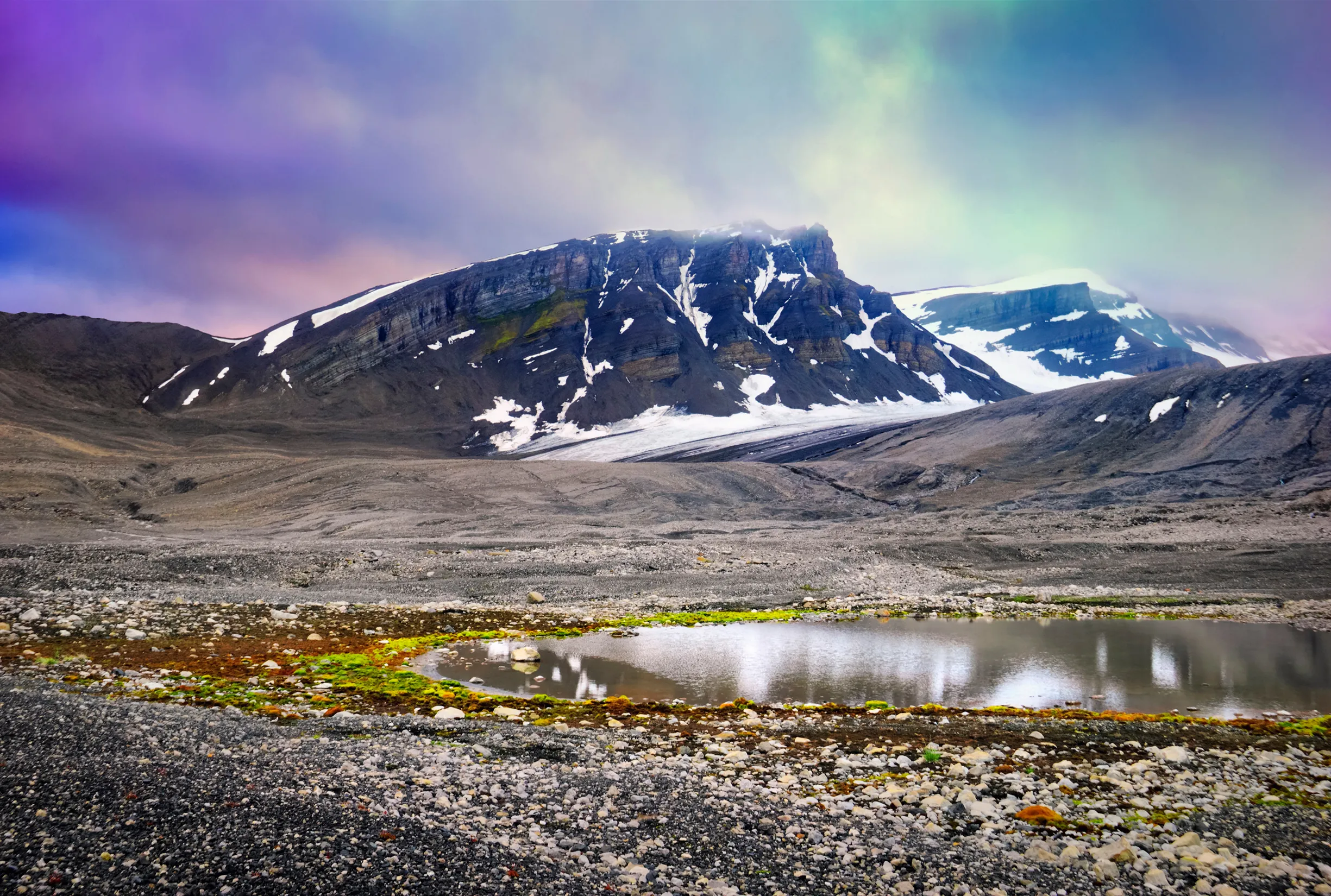 Beautiful scenic view, black rock, snow, pebble and small glacial lake with moss at the background of colorful dramatic sky near Barentsburg, Norway, Spitsbergen island, Svalbard and Jan Mayen