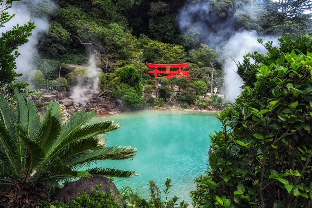 umi jigoku or sea hell taken in beppu with steamy hot springs geyser steaming off the cobalt water. Red torii gates nearby the geyser. Taken in Beppu, Japan