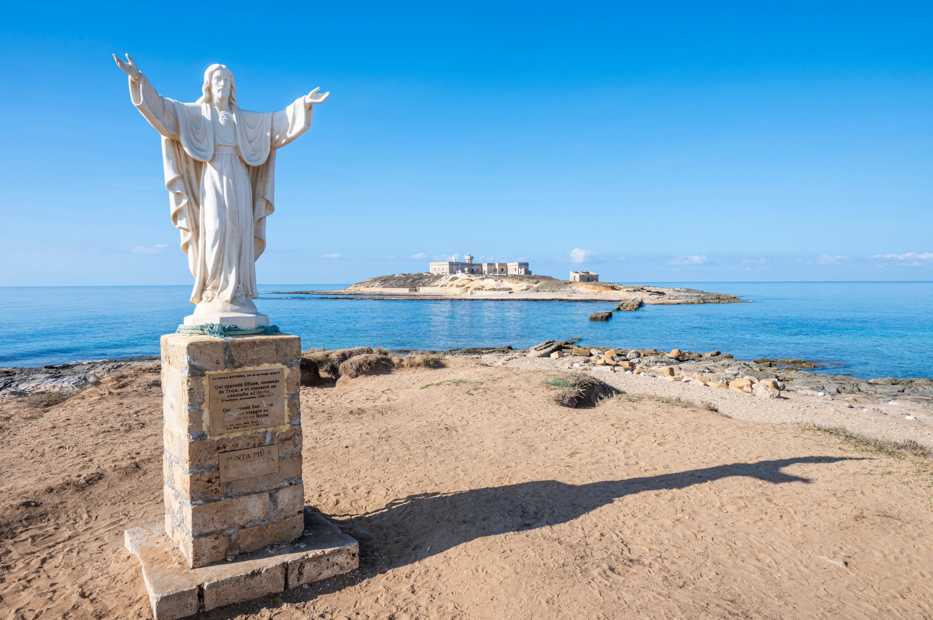Portopalo, Italy - 09-14-2022: The statue of Christ Redeemer in Portopalo with the Island of Correnti in background