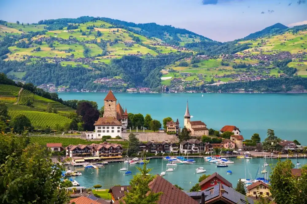Spiez Castle and the charming village of Spiez, with Thun Lake and lush green hills in the background, captured on a clear summer day in Switzerland. Spiez Castle and the charming village of Spiez, with Thun Lake and lush green hills in the background, captured on a clear summer day in Switzerland.