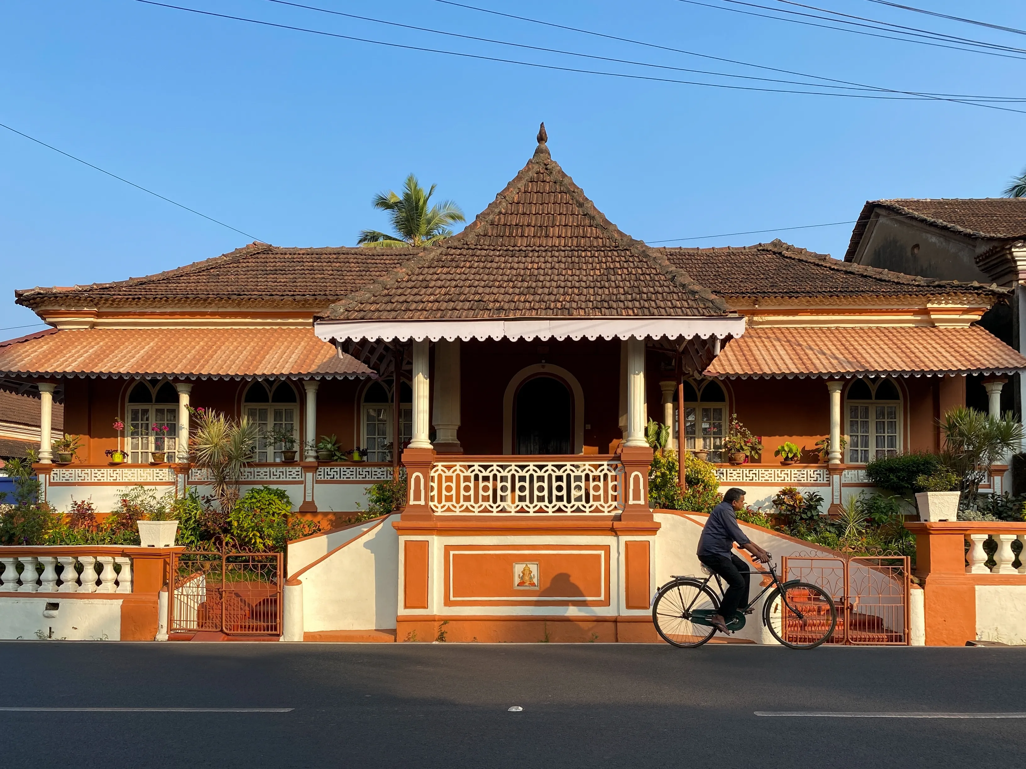 Margao, India - January 21 2023: A man riding a bicycle past a beautiful old house with traditional architecture in South Goa.