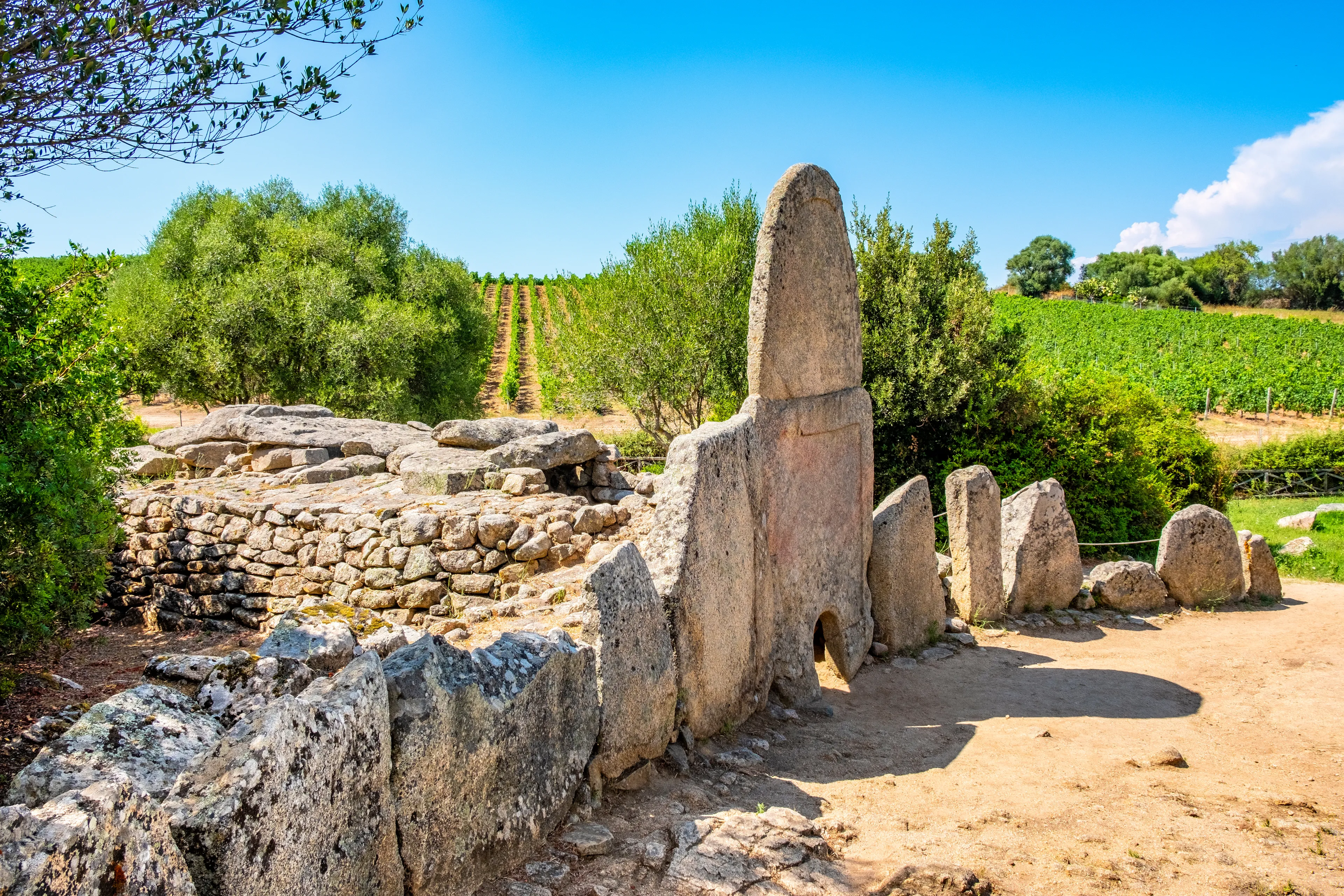 Arzachena, Sardinia / Italy - 2019/07/19: Archeological ruins of Nuragic necropolis Giants Tomb of Coddu Vecchiu - Tomba di Giganti Coddu Vecchiu - with front grave stones of Neolithic cemetery