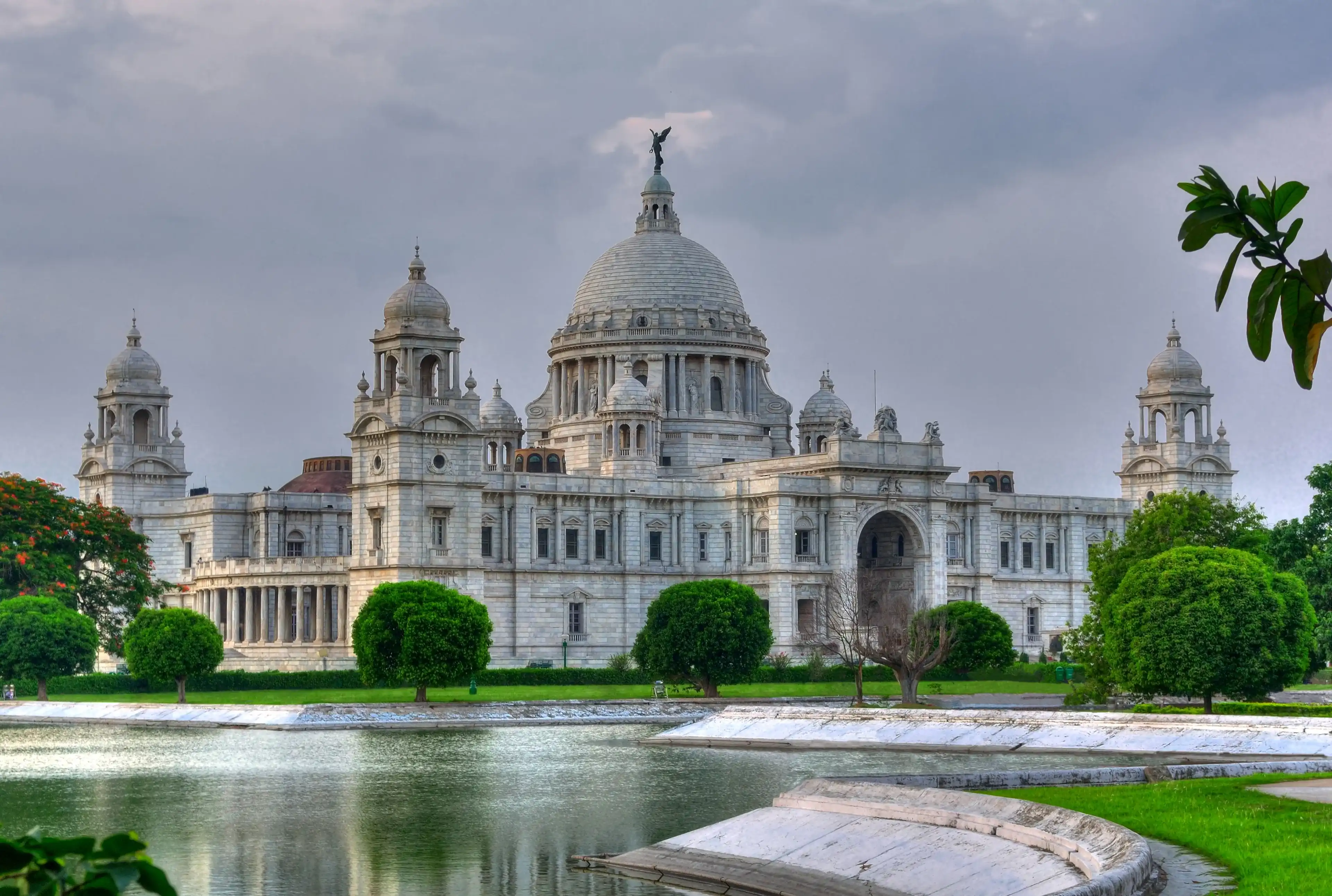 Landmark building of Calcutta (aka Kolkata), Victoria Memorial Hall with Queen's Garden in the foreground, pond, white Marble, cloudy sky