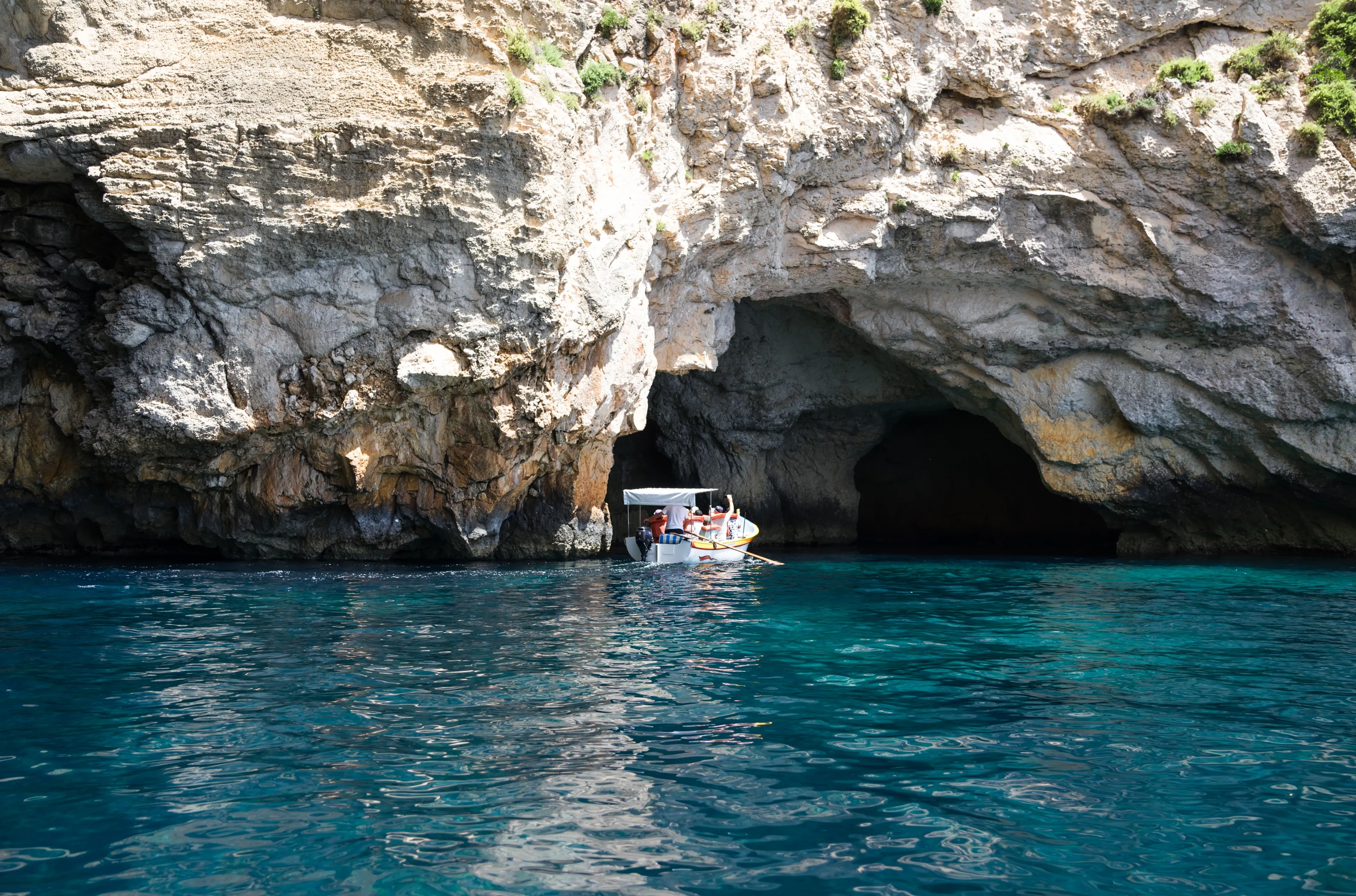 Il-Qrendi, Malta - July 18 2023: Magnificent scenery of Blue Grotto sea caverns from sea level close to Wied iz-Zurrieq. Hot summer day. Boat with tourists.