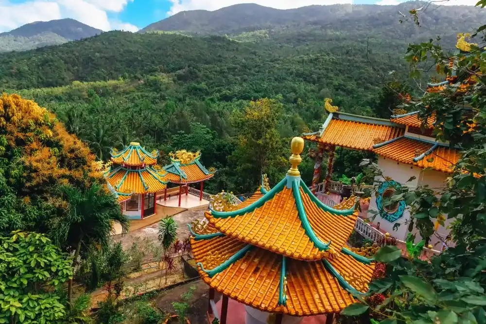 Beautiful view of Chinese Sangthom Temple of the Goddess of Mercy Shrine in Chaloklum, Ko Pha Ngan, Thailand Showing the ornate, orange roof of the main pagoda and the surrounding jungle.