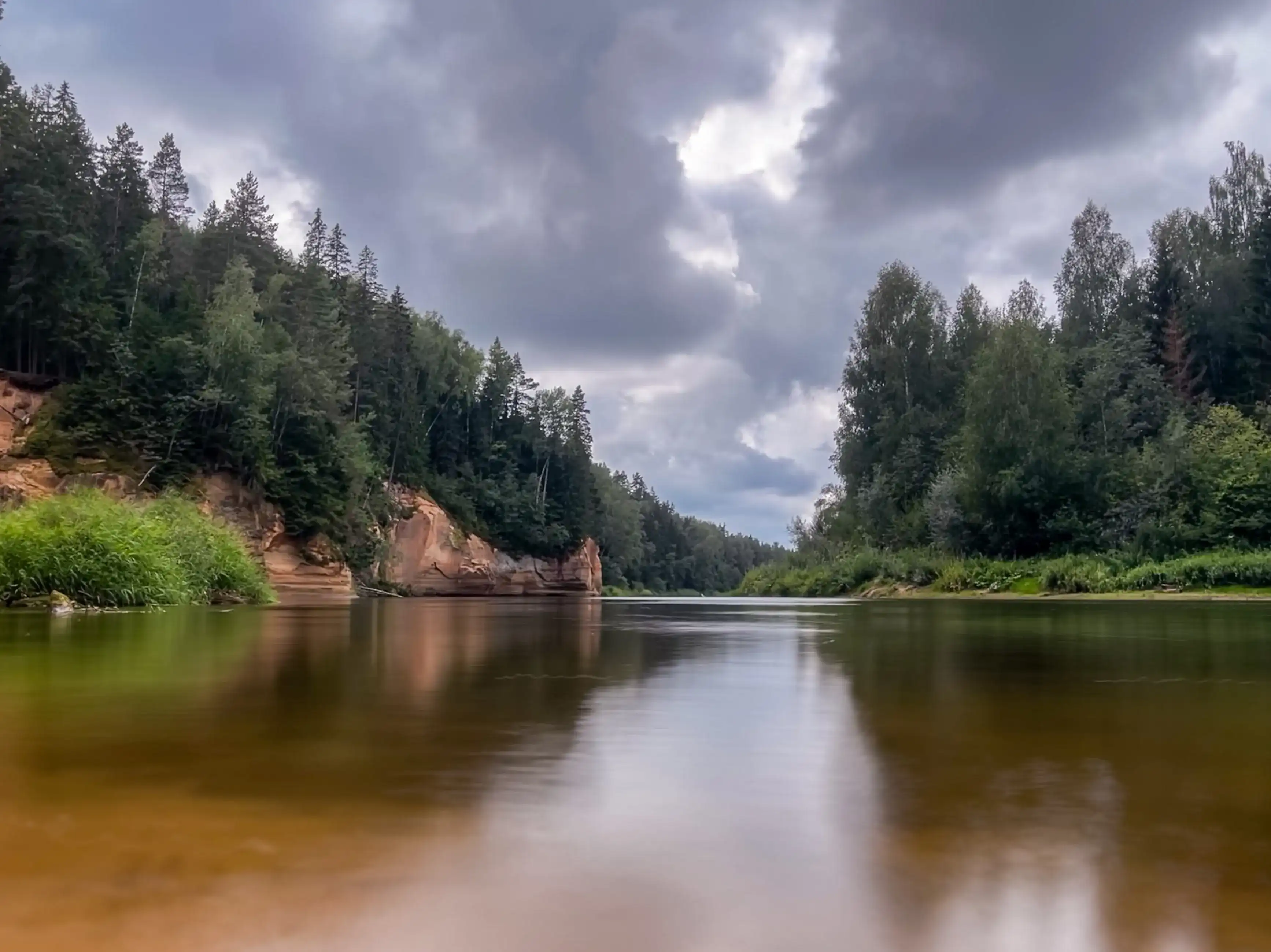 A tranquil river gracefully winds its way through a serene forest, its mirror-like surface reflecting the lush beauty of the surrounding woods. Erglu Klintis, Cesu novads, Latvija, Latvia