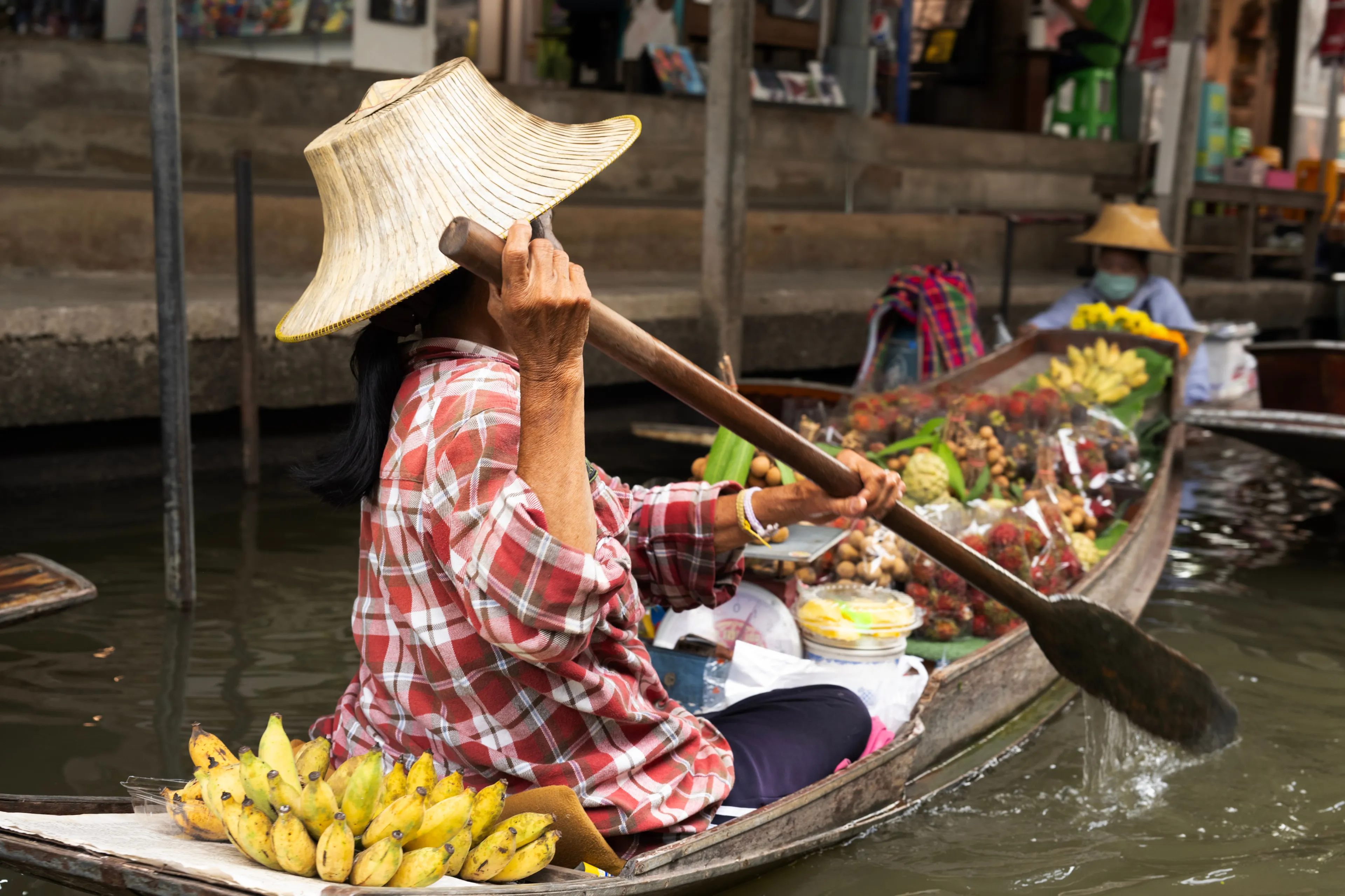Woman paddling boat at a vibrant floating market in Bangkok, Thailand