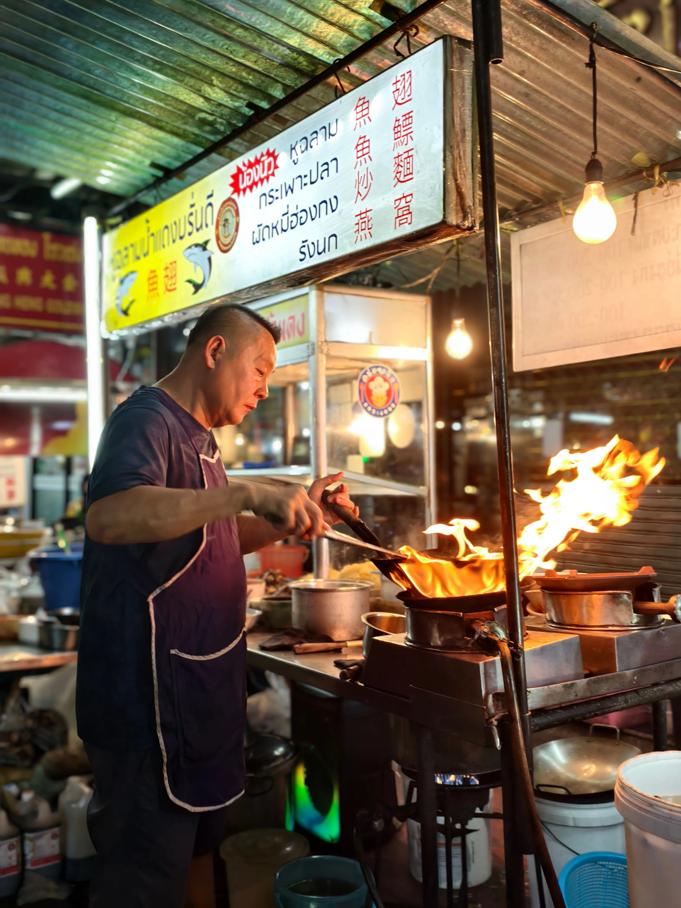 Chef flambéing at a vibrant Bangkok night market food stall