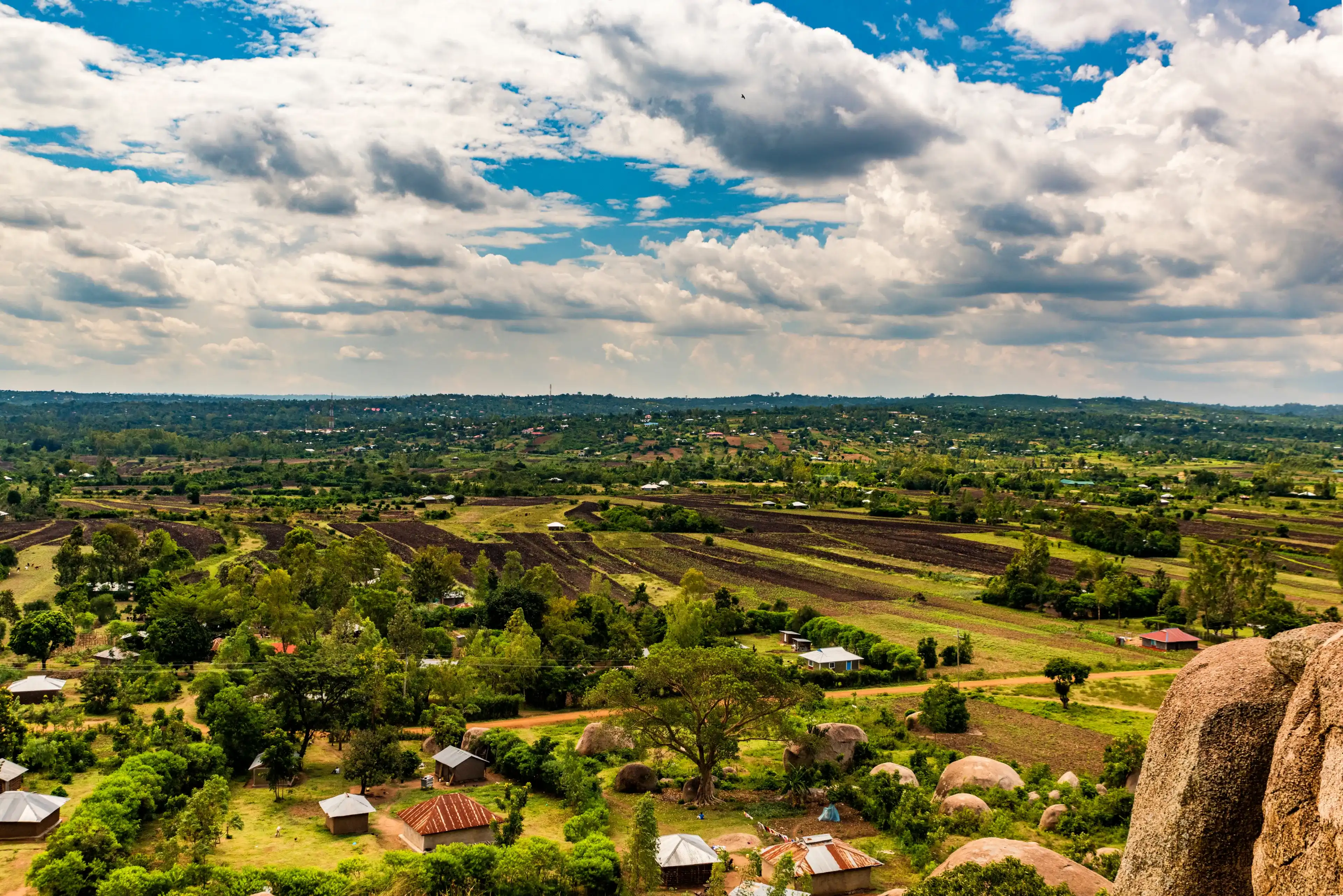 Aerial view from Kit Mikayi of flat rural land, farms, houses, agricultural land and a village in the distance. Partial bolder in foreground. Western Kenya, Africa. Copy space. 
