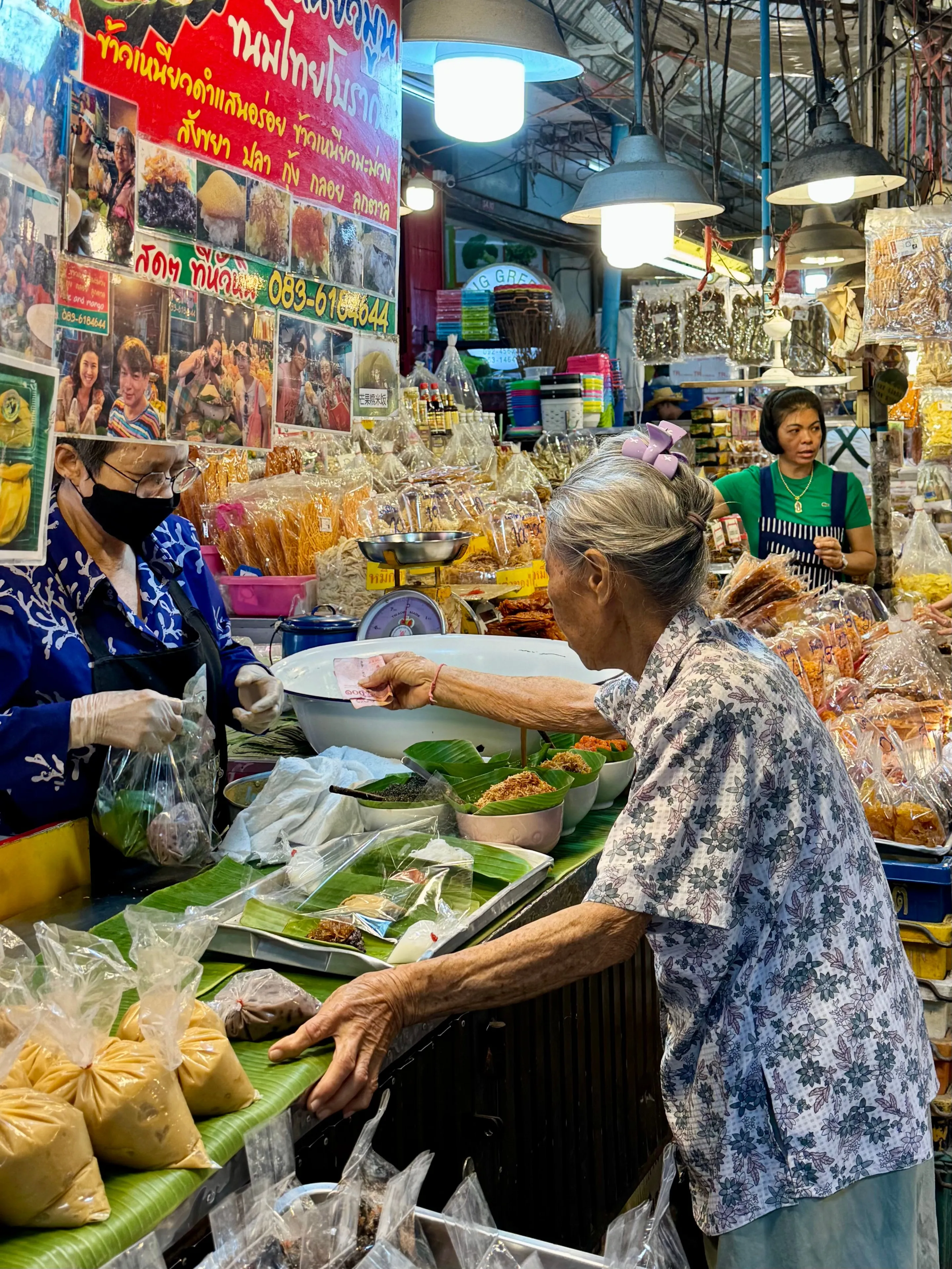 An elderly woman buys food in a vibrant Thai market, full of colors and local people.