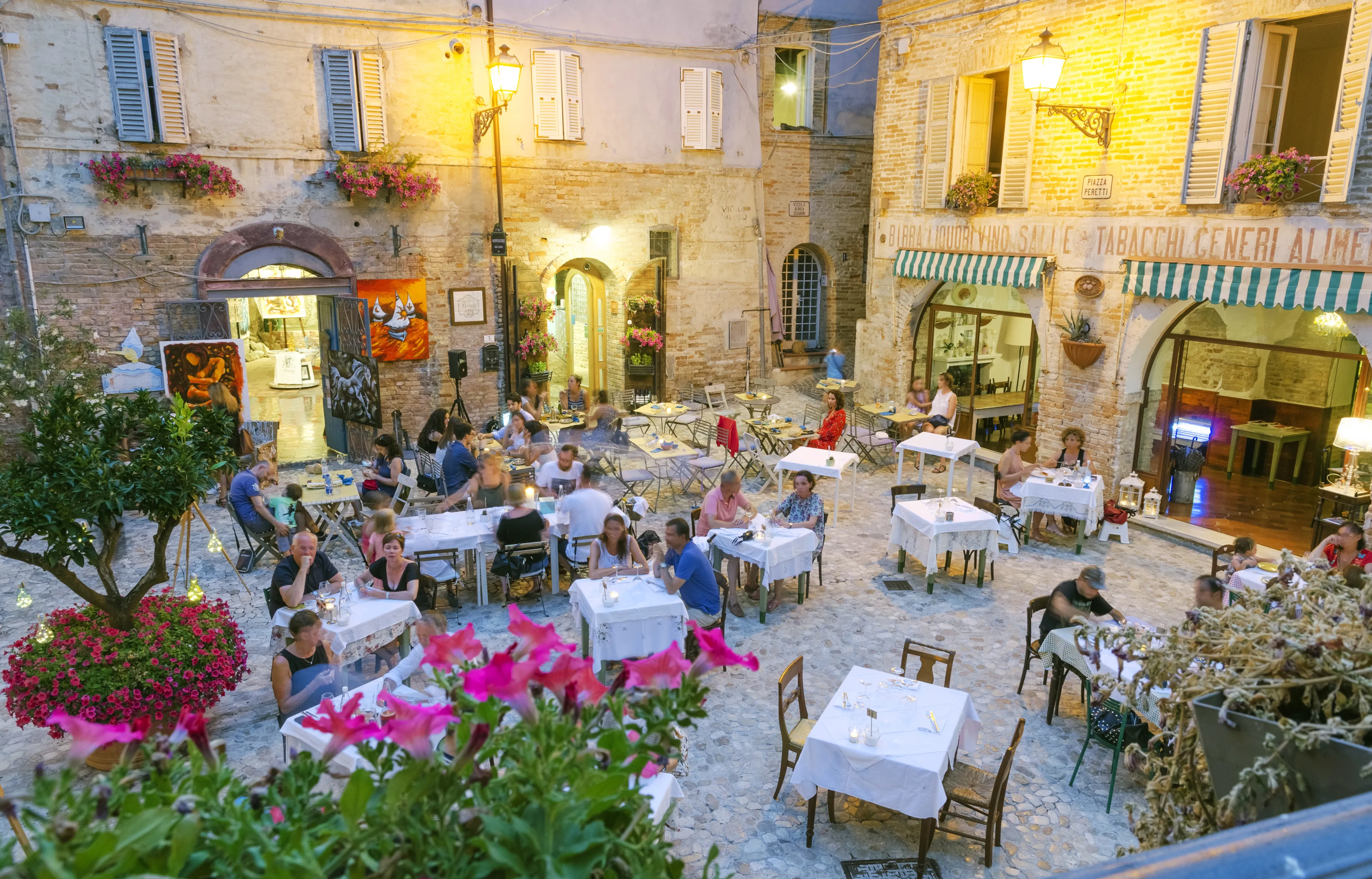 ITALY, Grottammare - July 12, 2017: An evening in Piazza Peretti. People eating and drinking in traditional restaurants with tables placed on a small stone paved square.