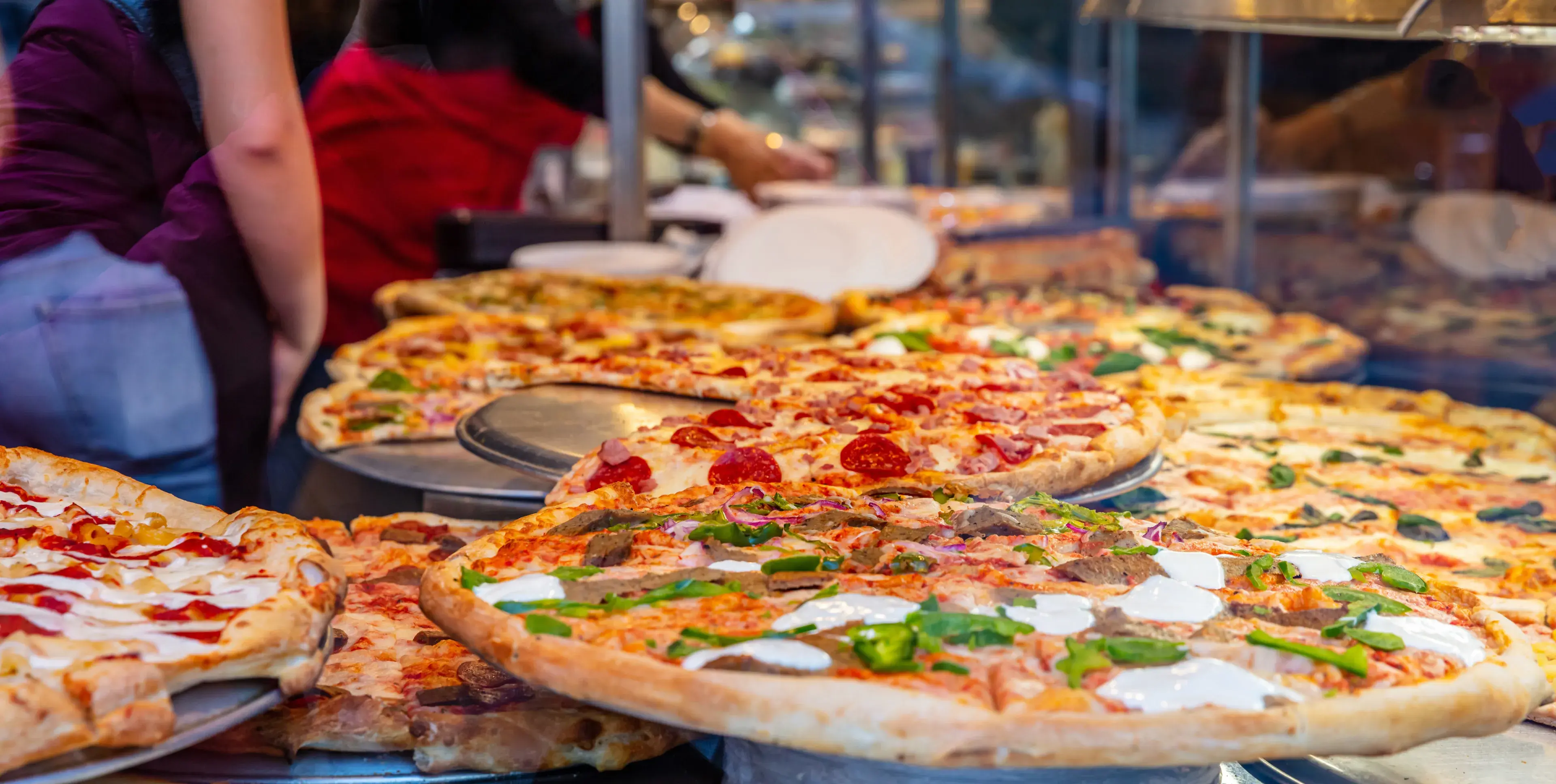 Pizzeria glass window. Variety of italian pizzas in a shop display, street food. Kitchen workers arranging the pizzas. Pizzeria glass window. Variety of italian pizzas in a shop display, street food. Kitchen workers arranging the pizzas.