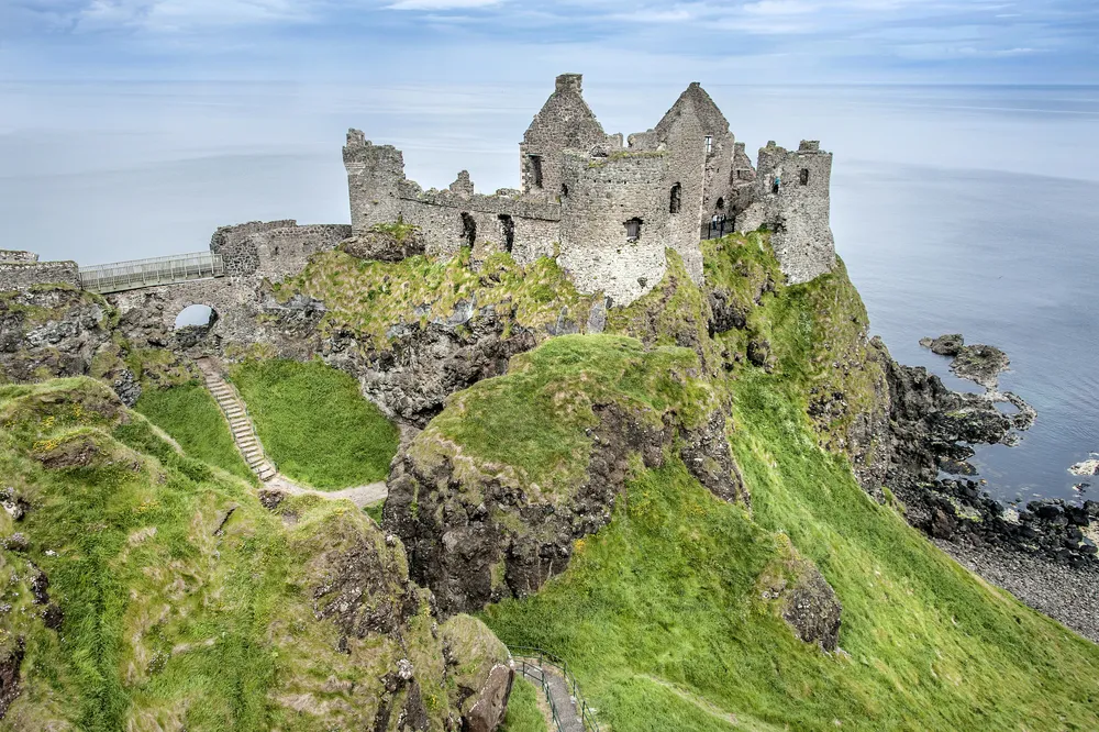 Northern Ireland, near Portrush: The famous old beautiful ruin of Dunluce Castle on green rocky hill with cliff coastline water ocean sea blue sky in the background. 
