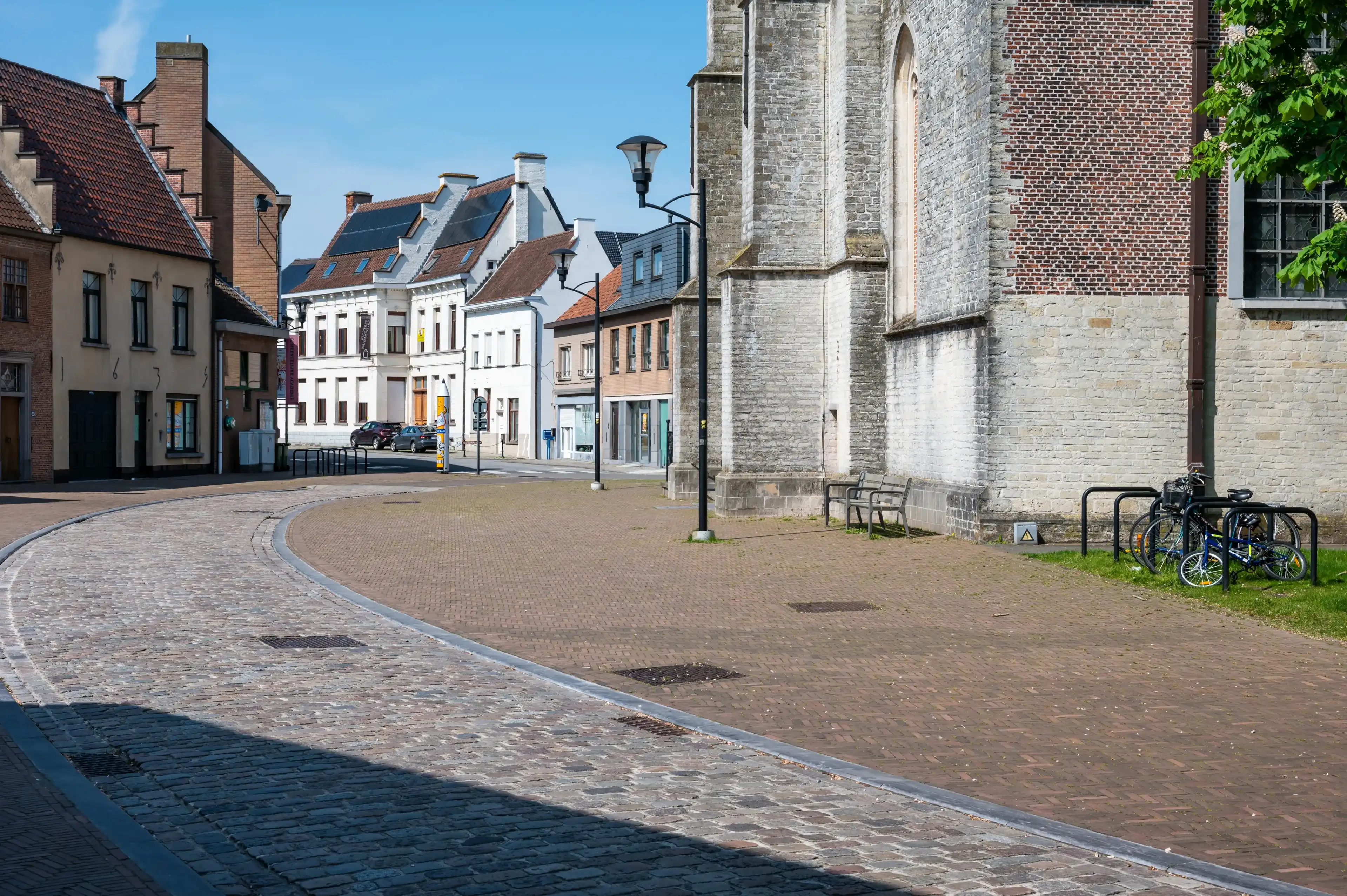 Waasmunster, East Flemish Region, Belgium - May 18, 2023 - Old cobble stone road, church and historical buildings at the old market square in the village center