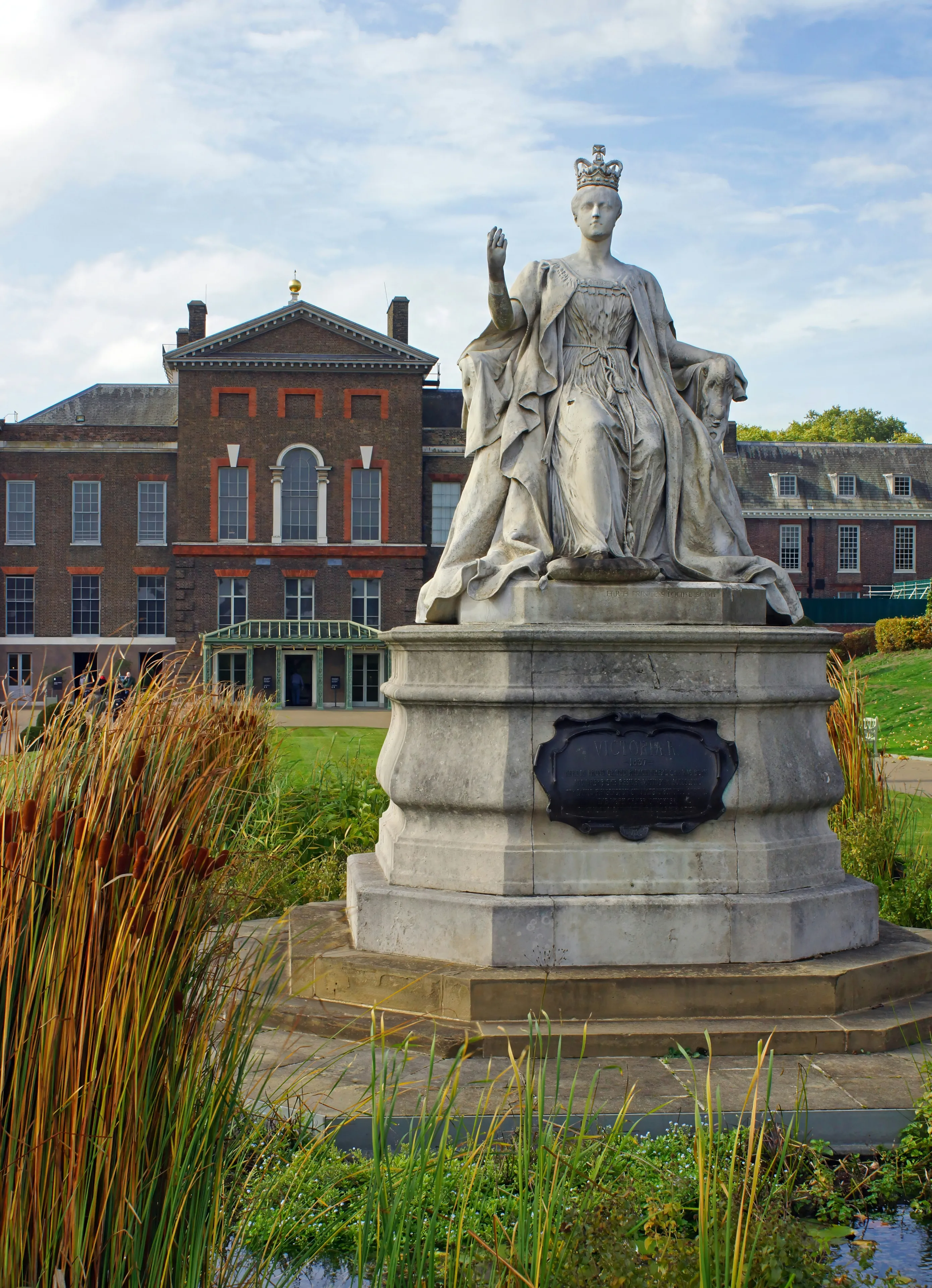 Statue of Queen Victoria in front of Kensington Palace in London on a partly cloudy autumn day.