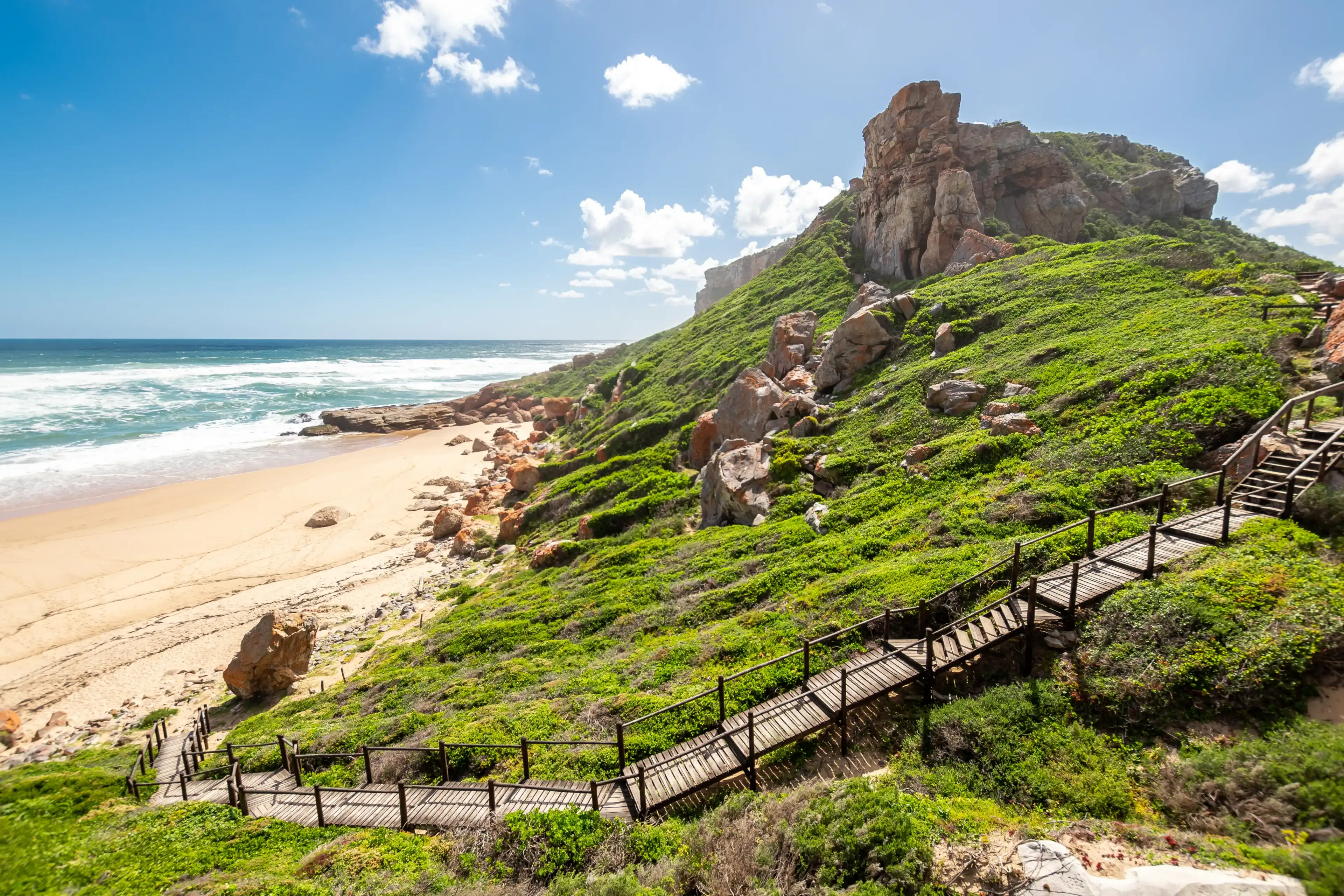 Landscape photo of a boardwalk with handrails going down to a deserted beach on a sunny afternoon with ocean and waves in the background. Shot in Plettenberg Bay, Western Cape, South Africa. Landscape photo of a boardwalk with handrails going down to a deserted beach on a sunny afternoon with ocean and waves in the background. Shot in Plettenberg Bay, Western Cape, South Africa.