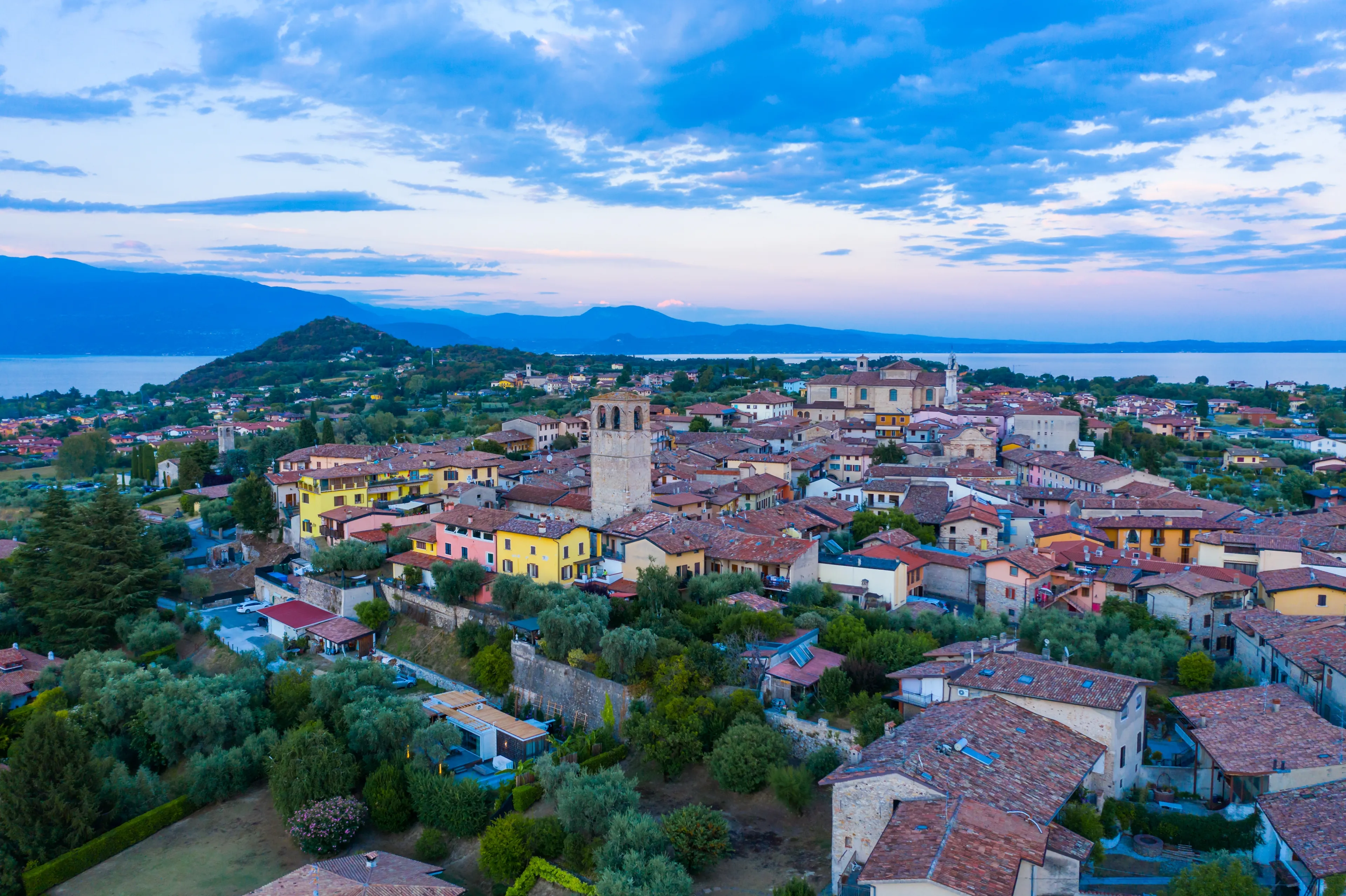Aerial view of village near Lago di Garda Italy. Beautiful sunset light. Flying close to the church tower revealing Lago di Garda on the horizon. Manerba del Garda town in Brescia Italy. 