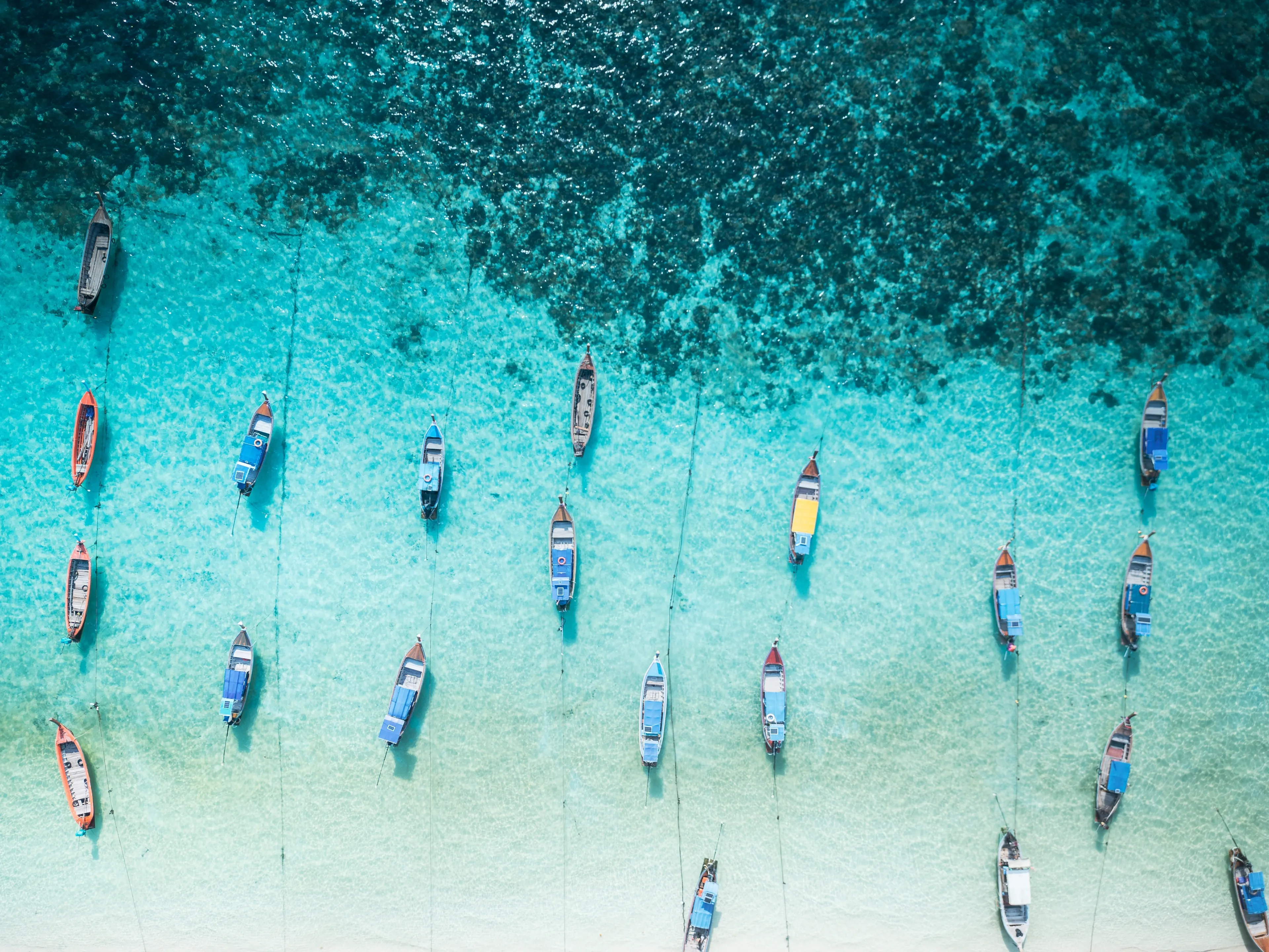 Background of a group long-tailed local boats or Hua Tong waiting transport for tourist on beach at Koh Lipe, Satun, Thailand. Aerial top view from drone see the coral reefs under Andaman sea blue.