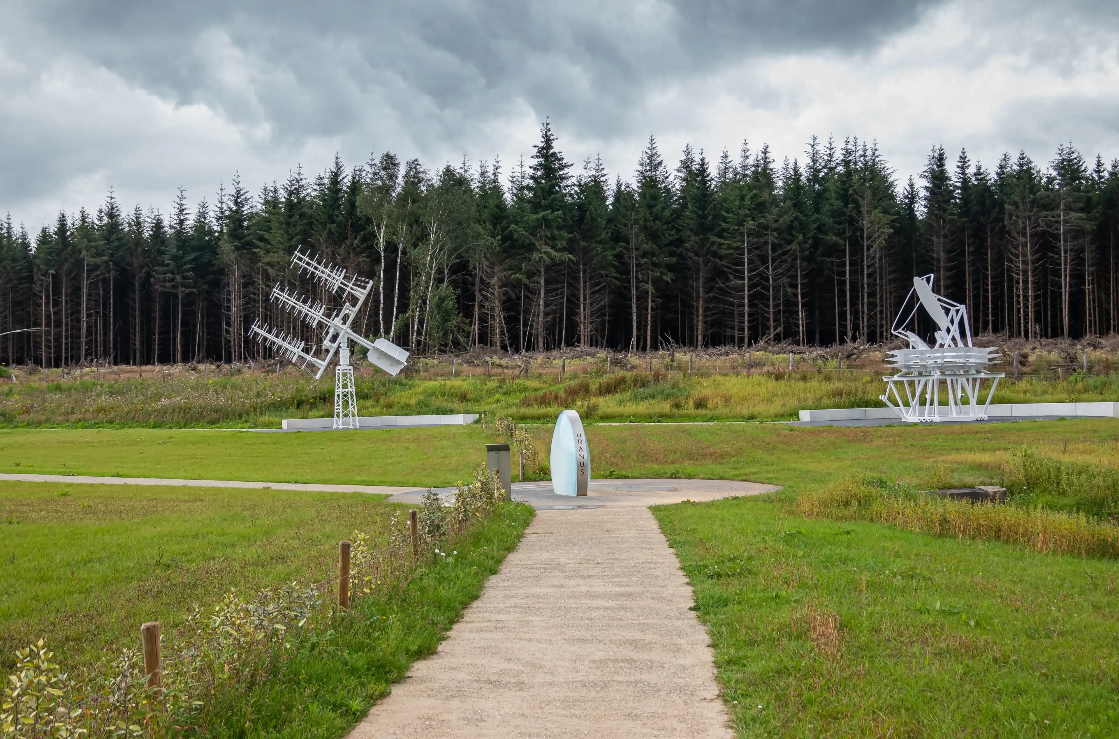 Transinne, Wallonia, Belgium - August 10, 2021: Euro Space Center. Uranus symbol and the Planck Mock Up and Yagi Antennas under rainy cloudscape. Dark green forest in back.