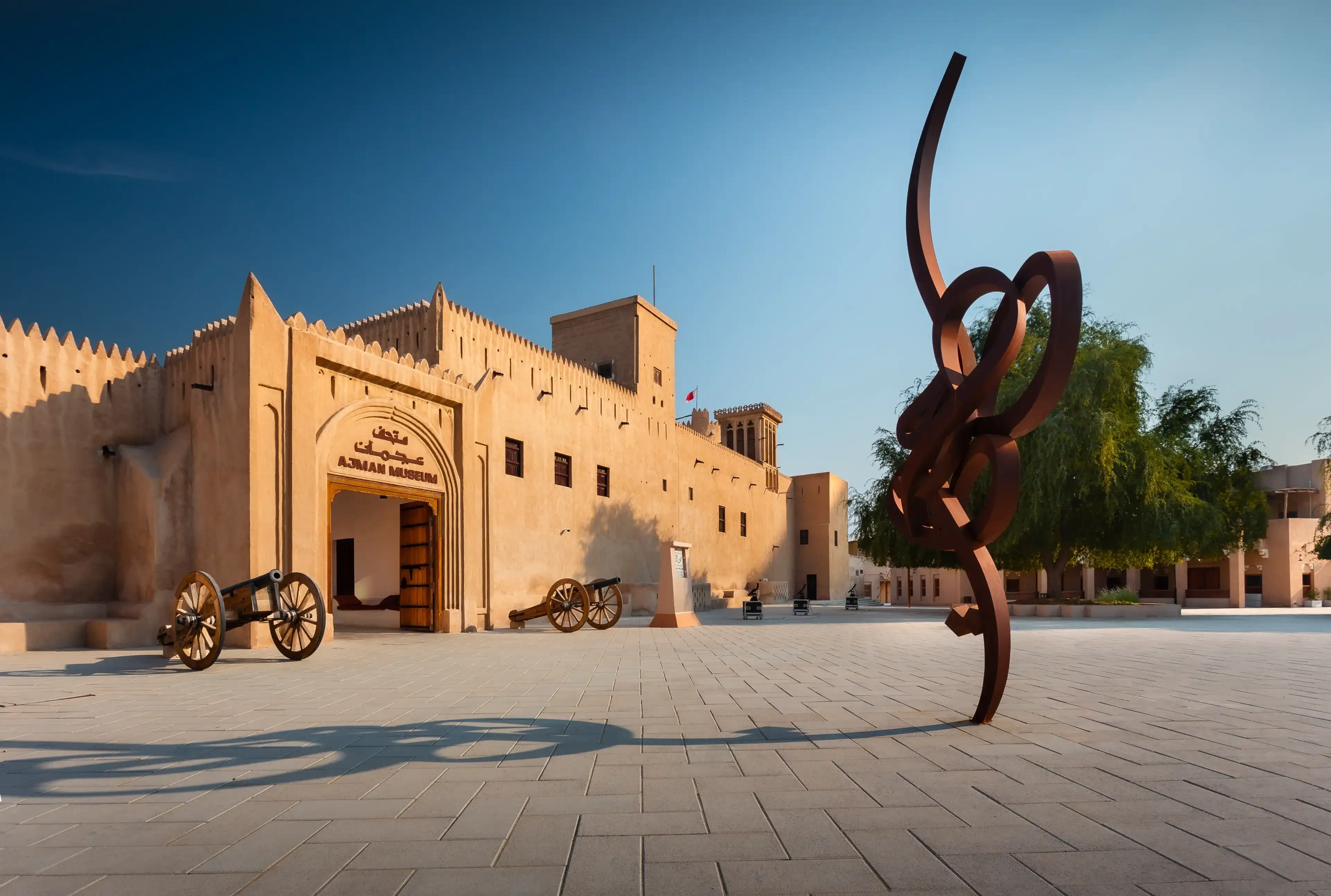 AJMAN, UAE, December 12, 2022: MUSEUM OF AJMAN gate during the afternoon with a calligraphic statue of ajman city and old ancient wooden cannons on the door