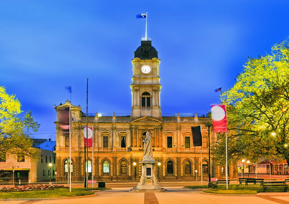 Facade of historic Town hall building in regional centre in Victoria state - Ballarat. Brightly illuminated at sunrise with Queen Victoria statue in foreground.
