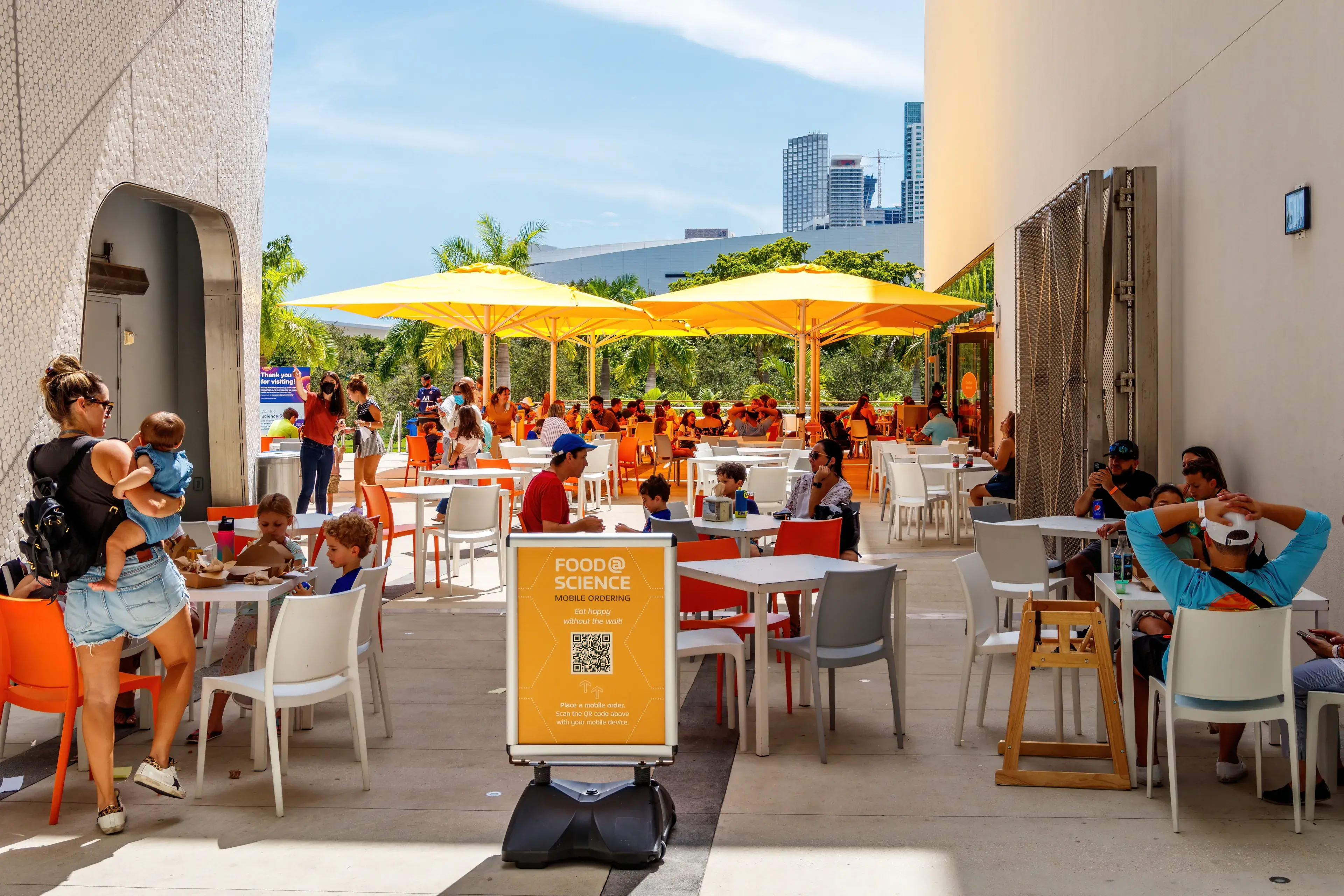 Miami, Florida, USA - September 25th, 2021 - Dining area for lunch, brunch and snacks at the Frost Museum color designed in yellow gold with umbrellas, tables, chairs and QR code signage for menu. Miami, Florida, USA - September 25th, 2021 - Dining area for lunch, brunch and snacks at the Frost Museum color designed in yellow gold with umbrellas, tables, chairs and QR code signage for menu.